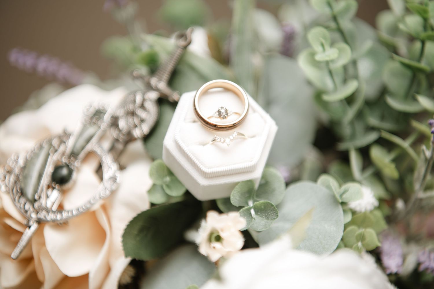 Wedding rings displayed on white hexagonal box surrounded by soft floral arrangements and eucalyptus leaves.