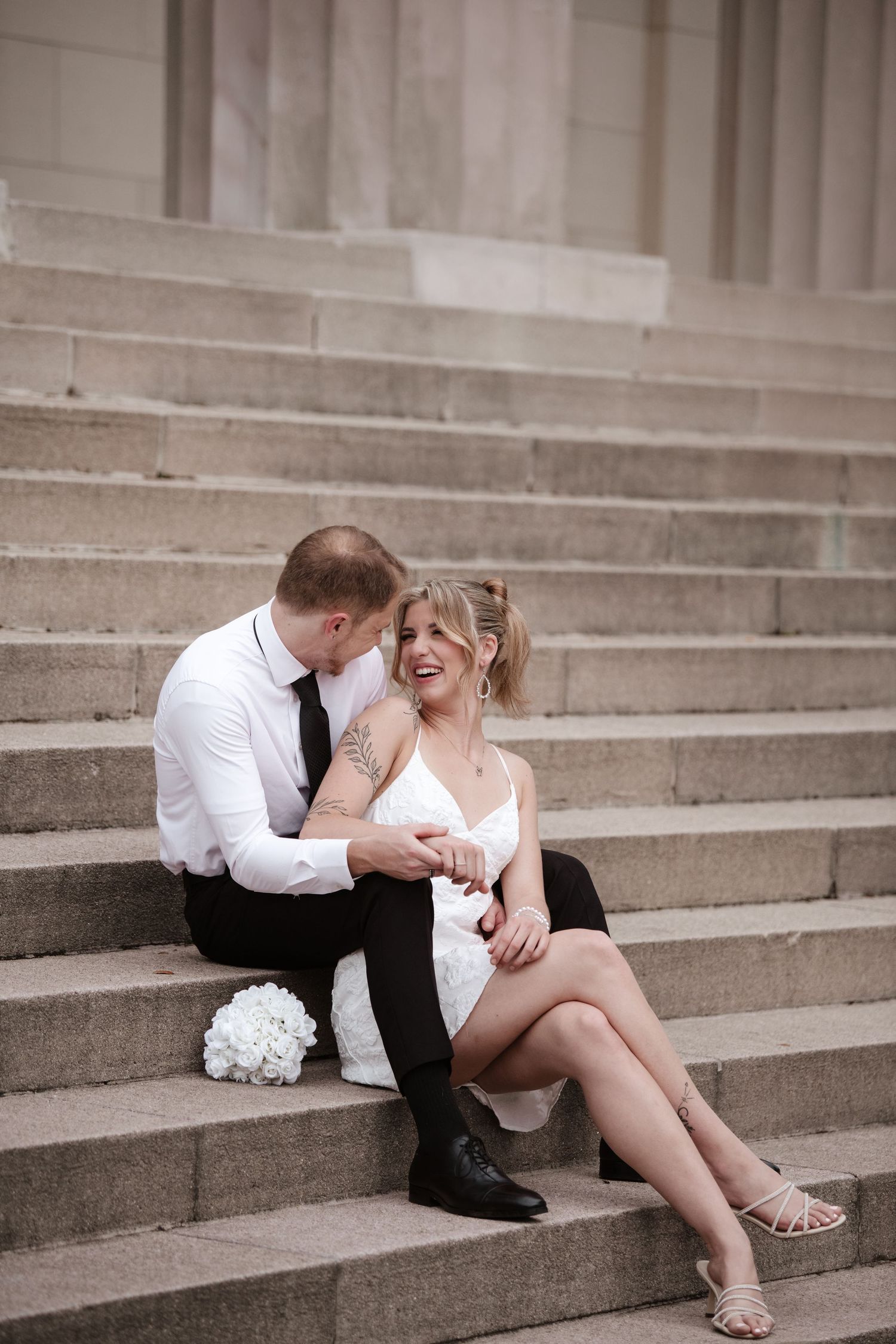 A couple shares an affectionate embrace while seated on architectural steps.