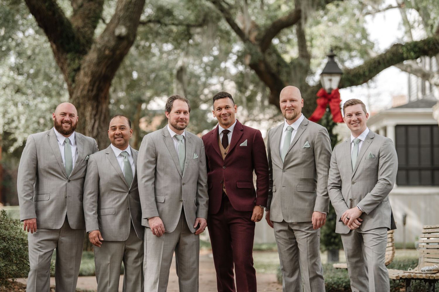 Groomsmen in gray suits and burgundy accents stand together for wedding party photos.