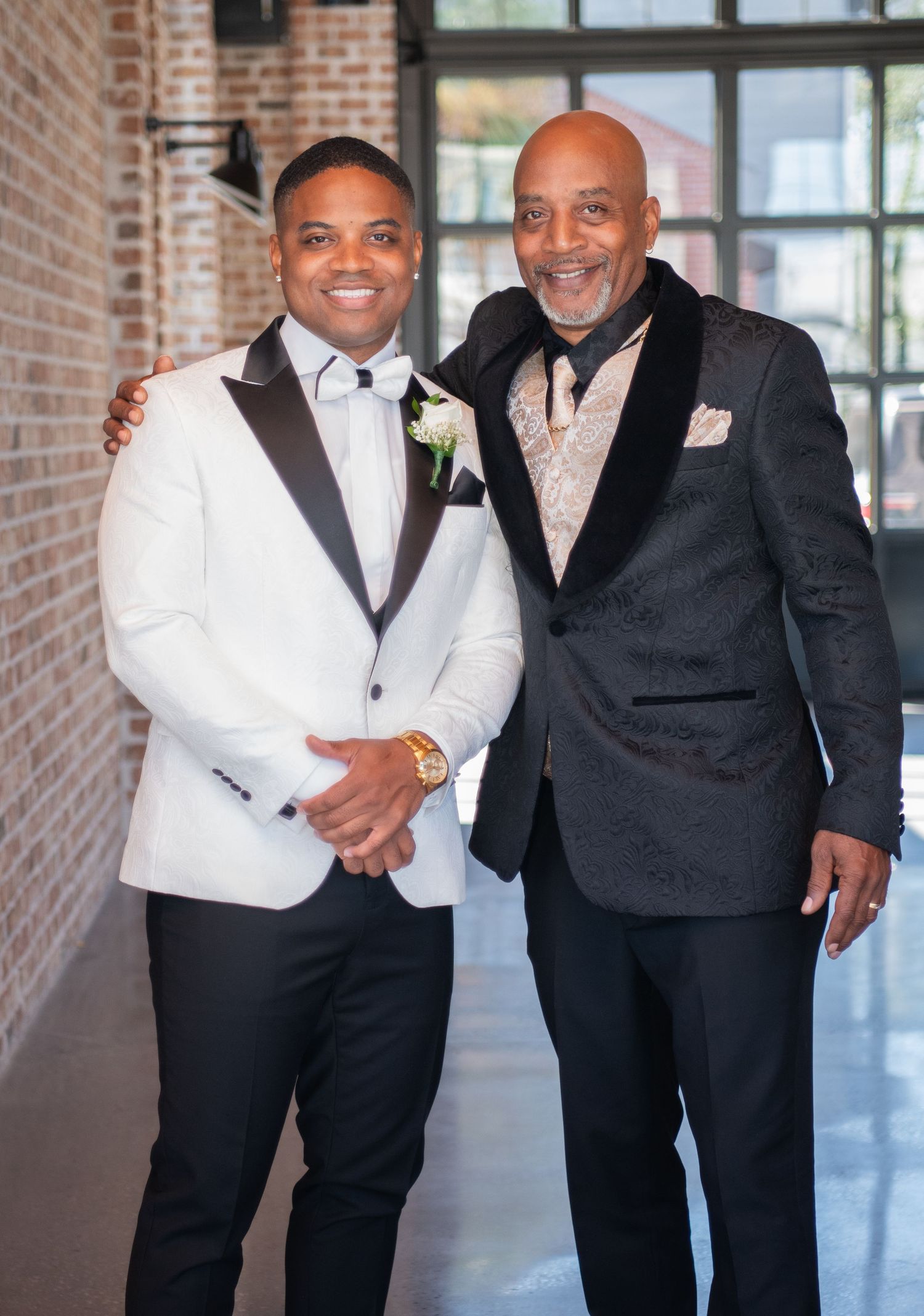 Two people in contrasting black and white formal attire share warm embraces at an event.