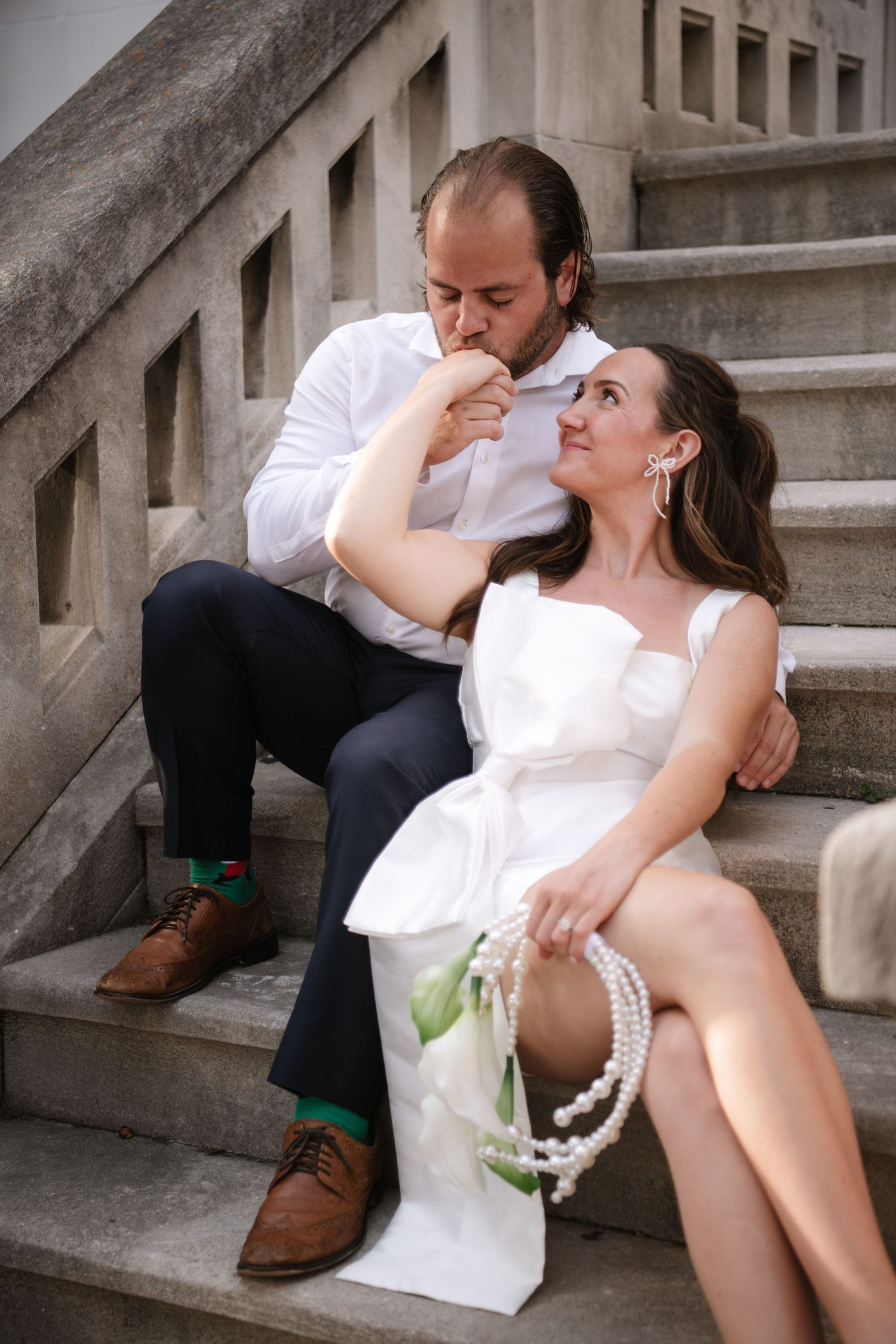 A romantic couple in white sits intimately on concrete steps during a photo session.