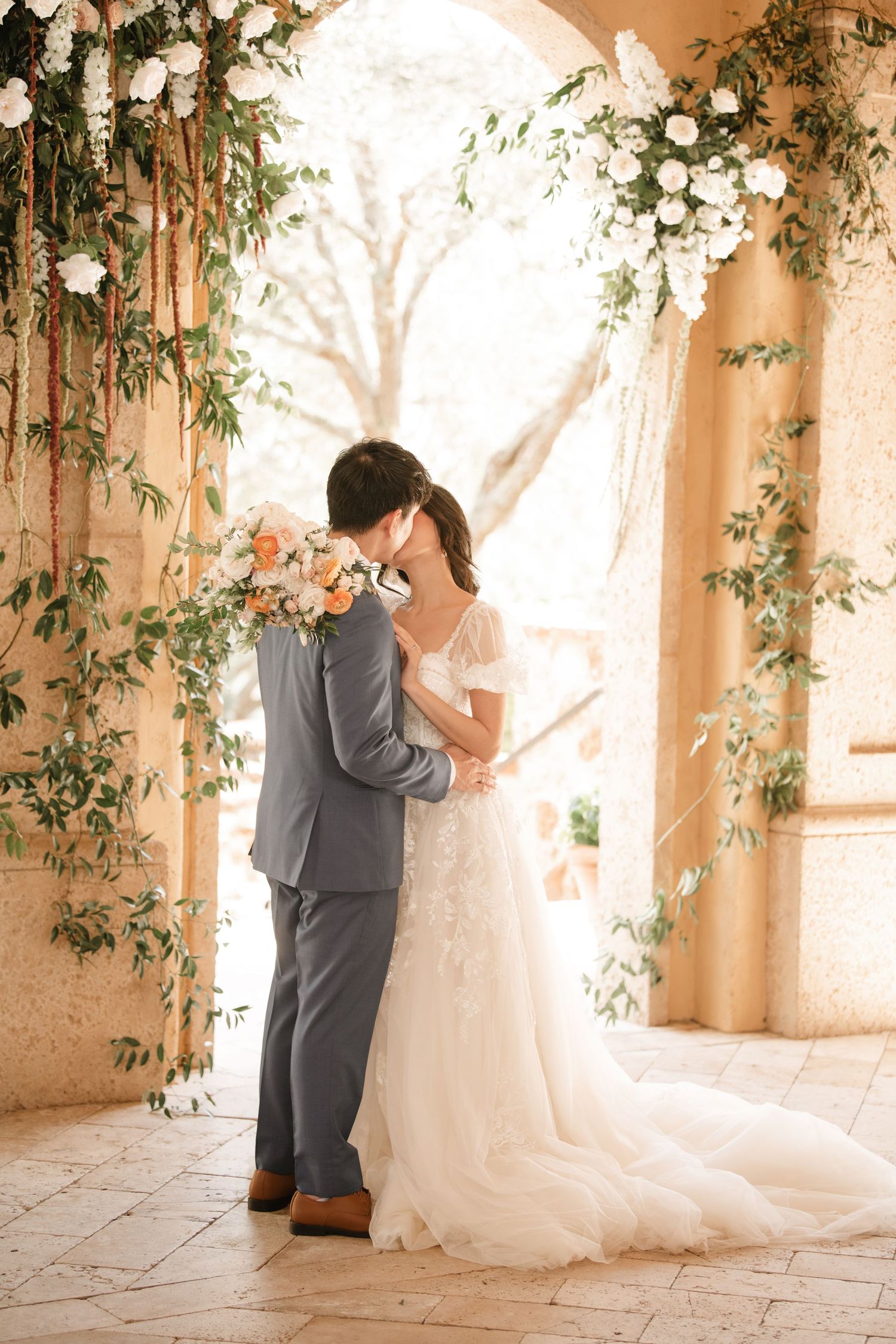 Romantic wedding dance sequence under stone arches decorated with white flowers and greenery.