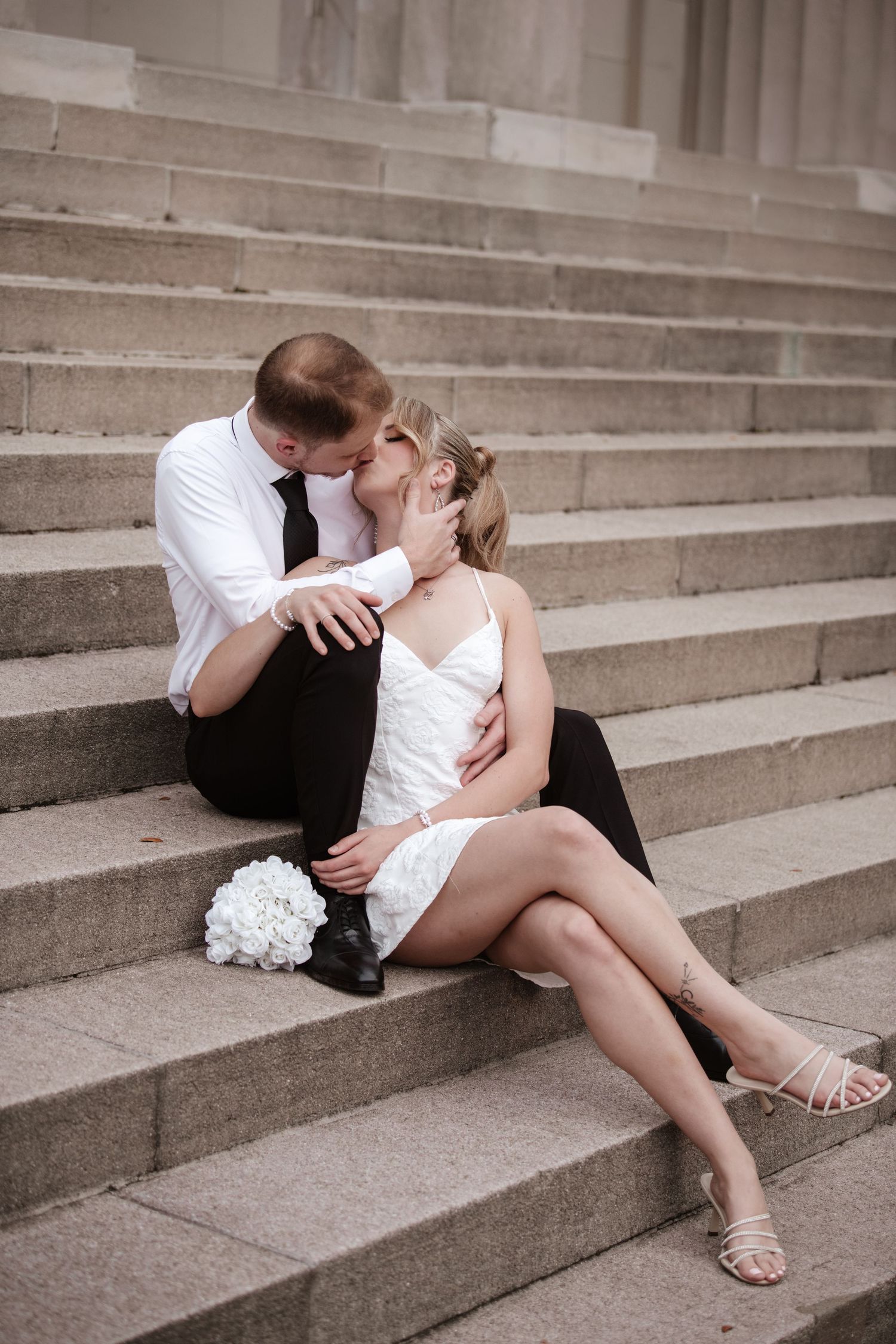 A romantic couple in formal attire shares an intimate moment while sitting on concrete steps.