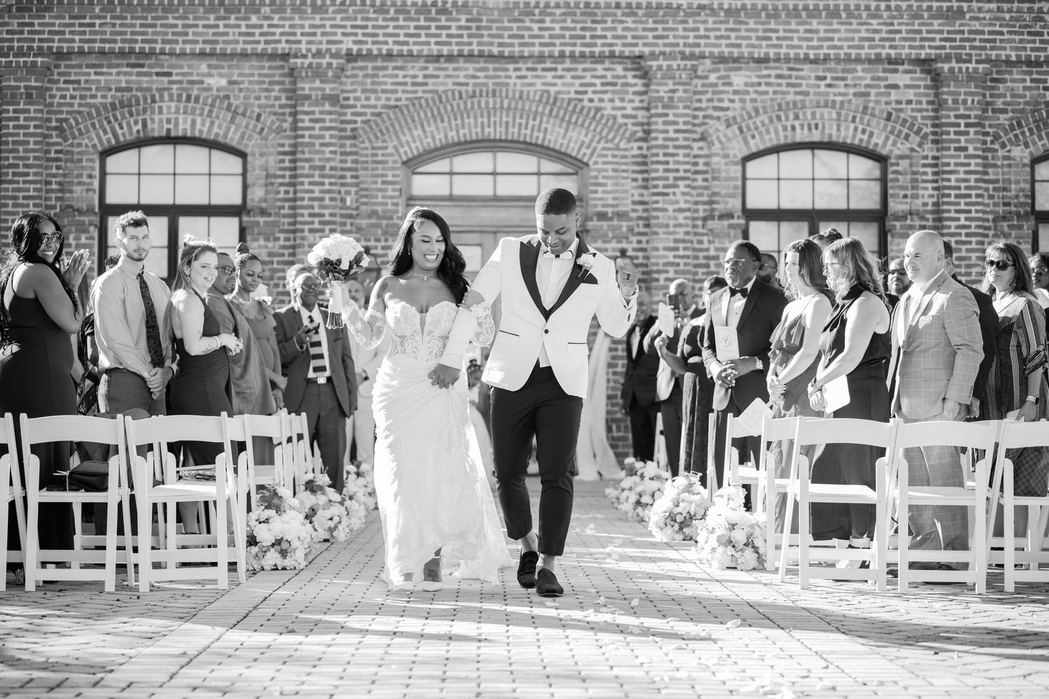 Black and white panoramic view of wedding ceremony setup with guests arriving.