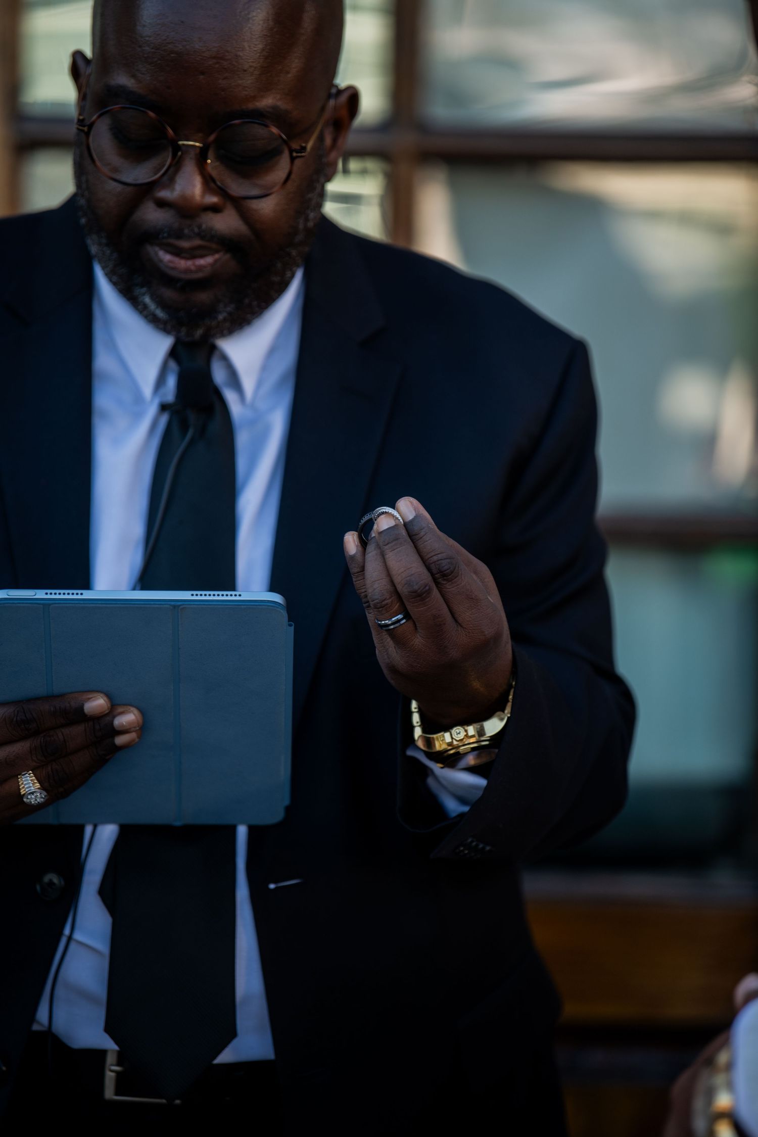 Person in formal suit holds tablet device during outdoor event.