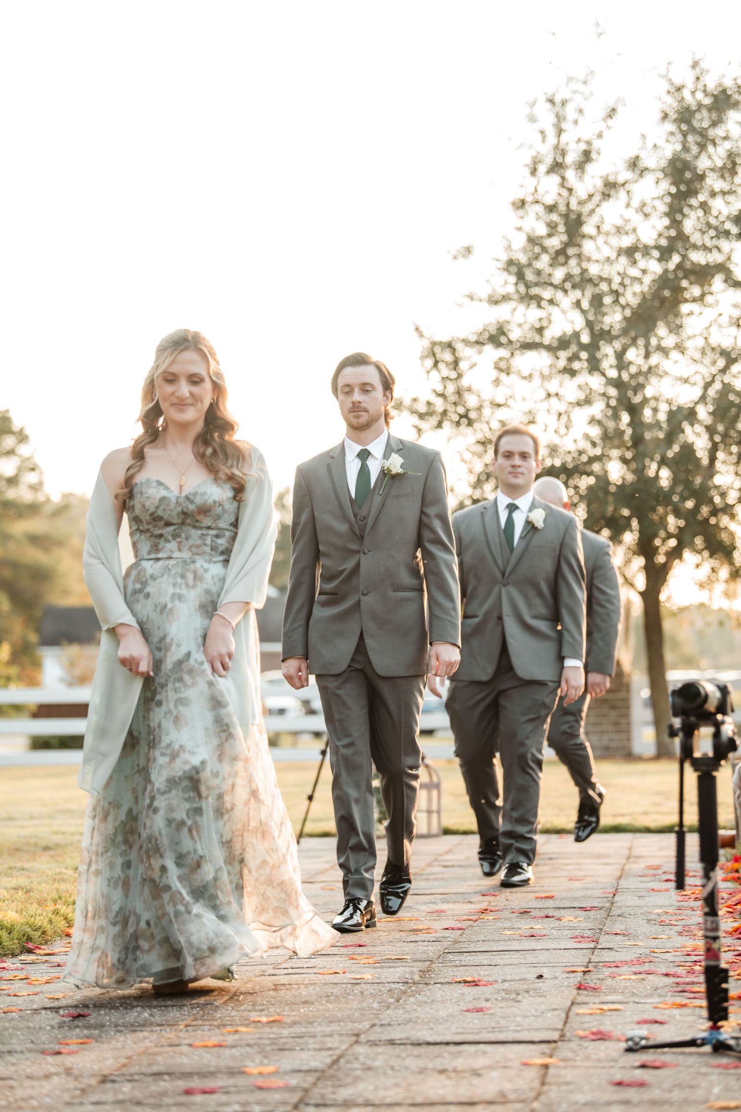 Wedding party walks along a decorated path at sunset with scattered rose petals.