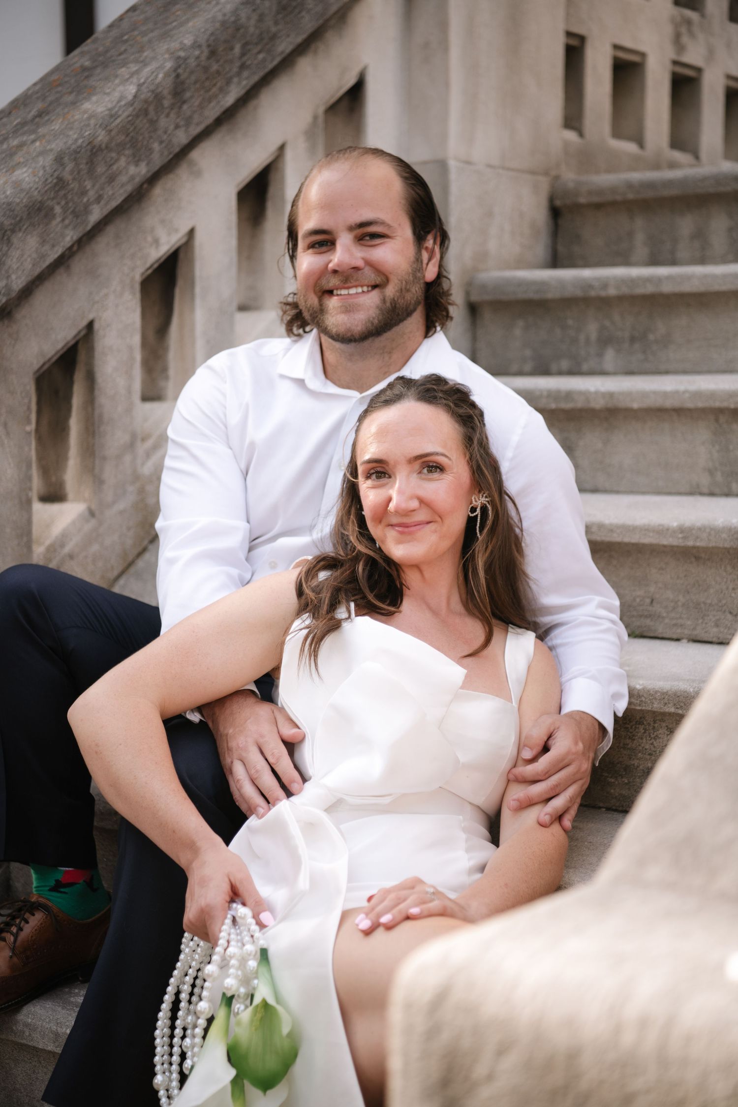 A couple in wedding attire share intimate moments while sitting on concrete steps in a series of romantic photos.