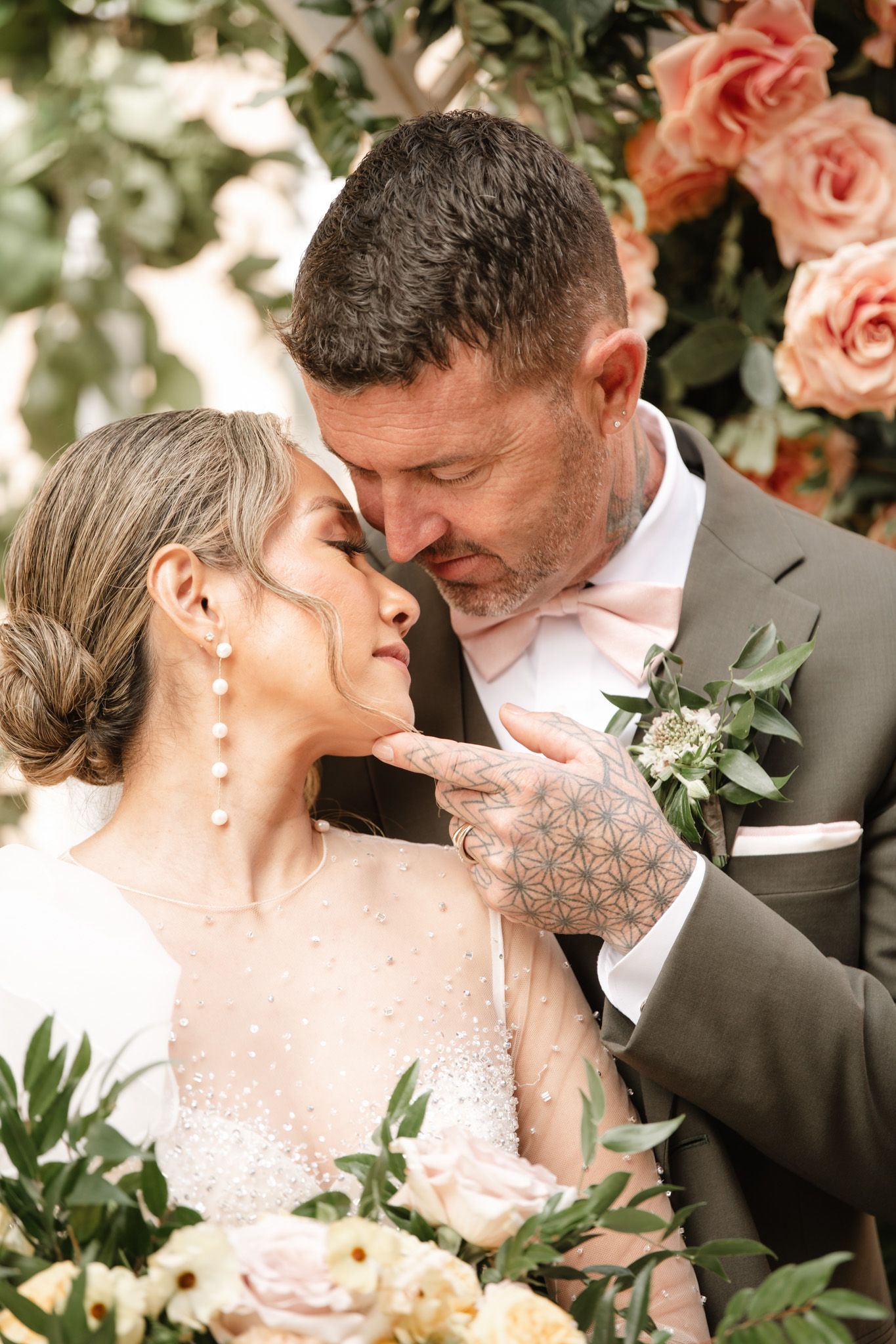 Romantic wedding moment surrounded by peach roses and greenery.