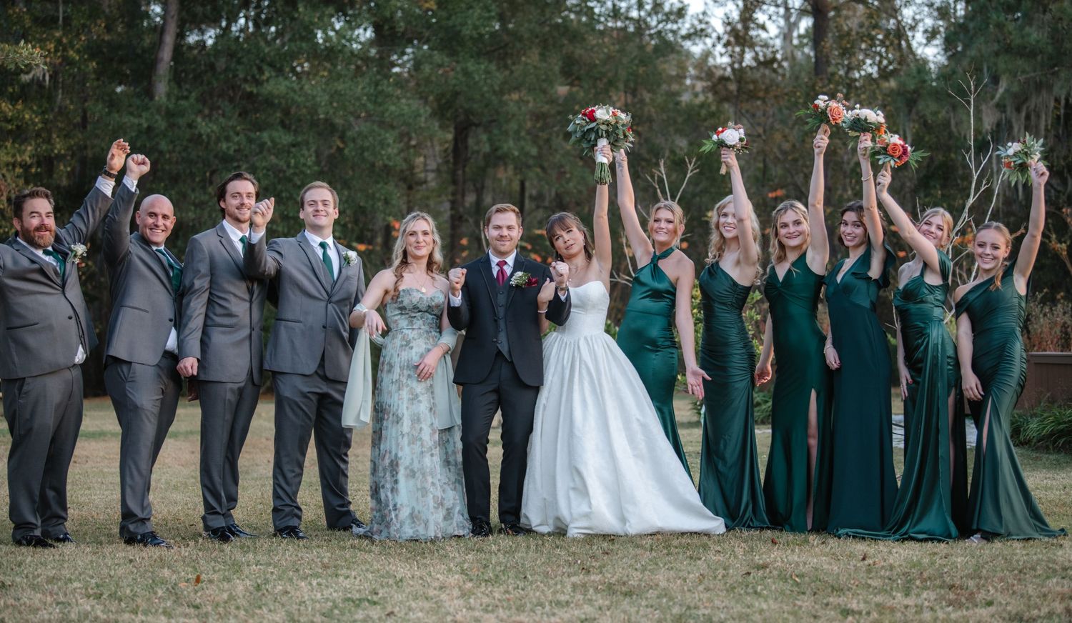 Wedding party members raise their arms in celebration during outdoor group photos.