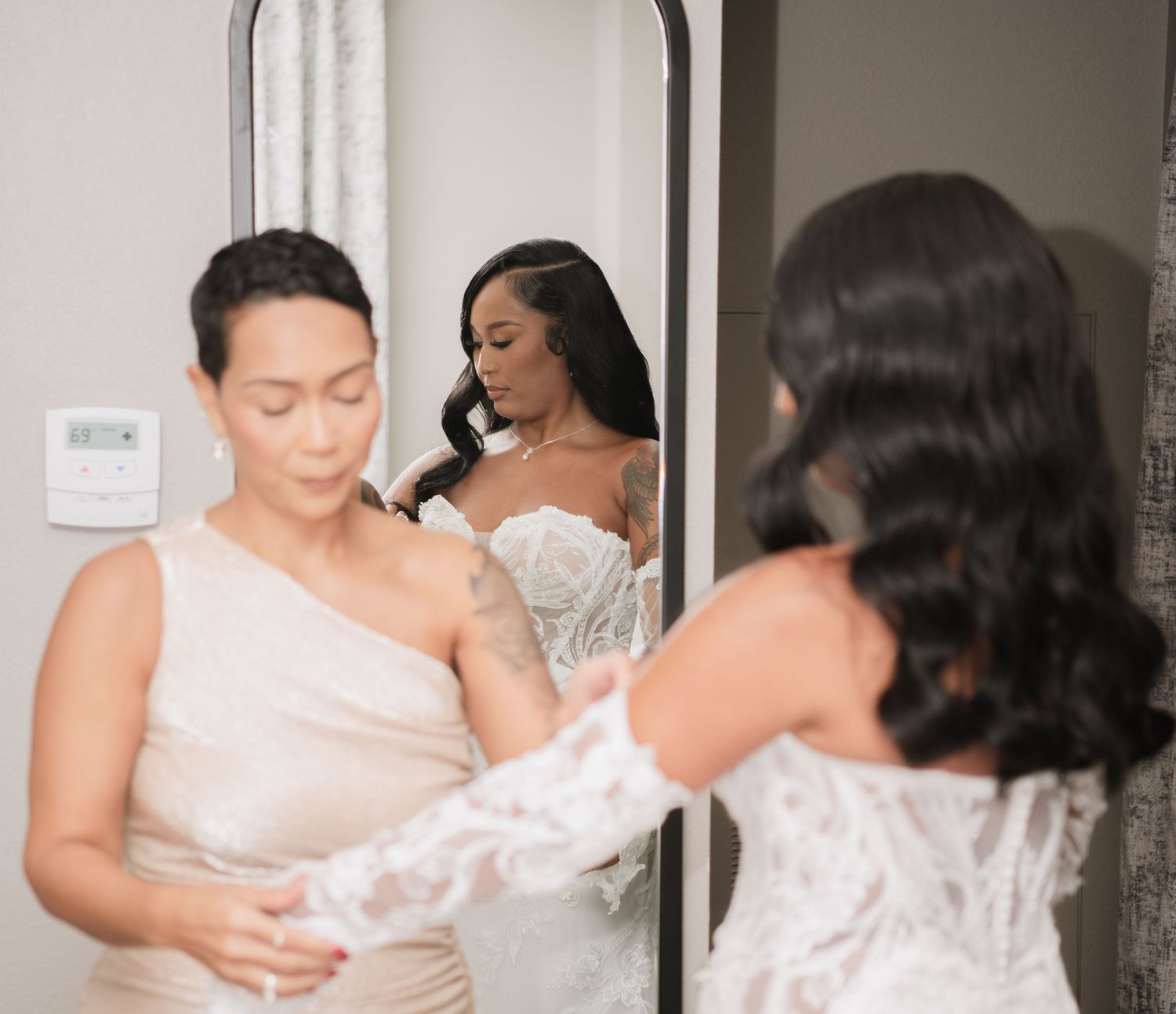 Wedding dress fitting scene with helpers assisting in final adjustments.