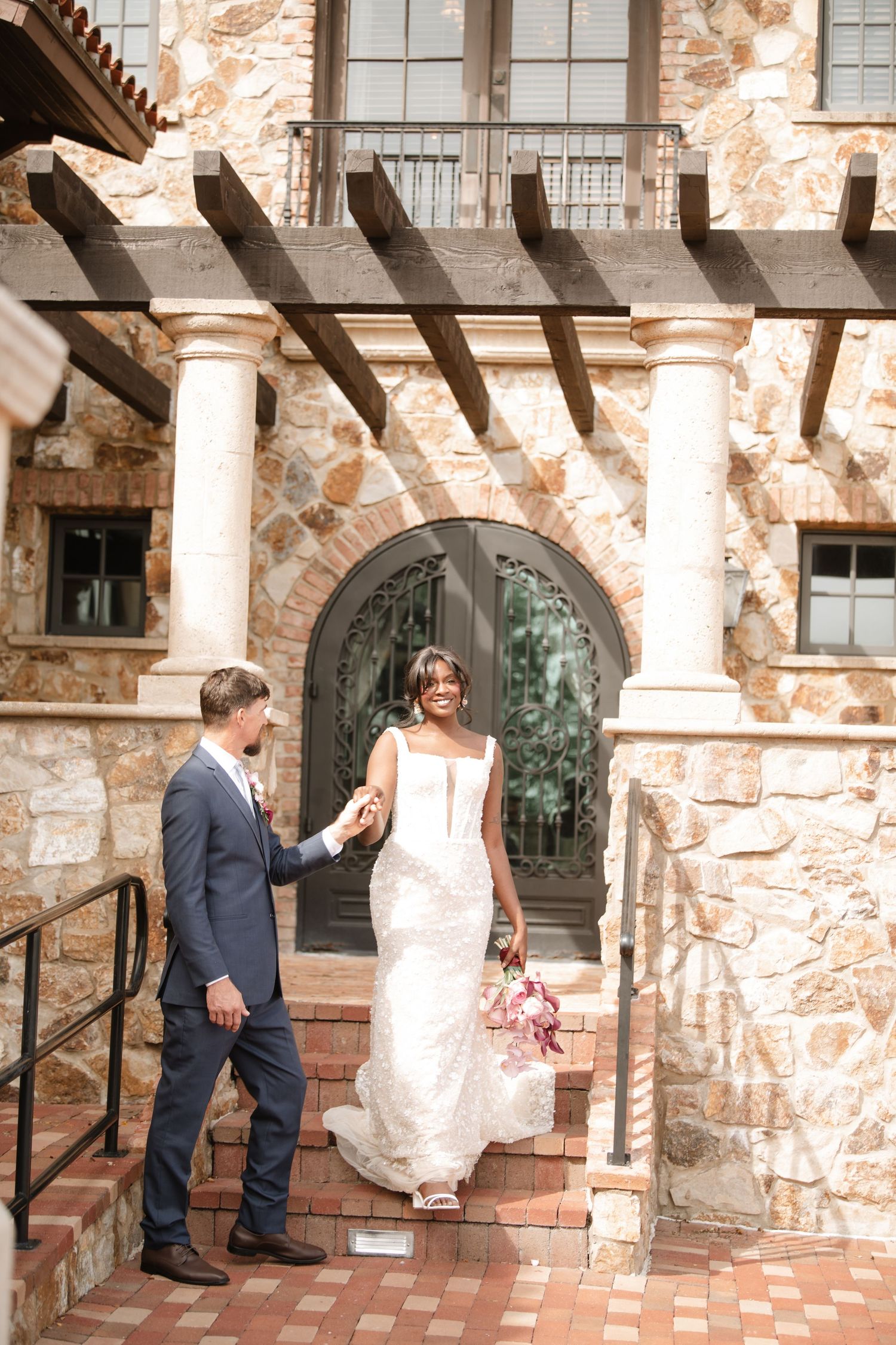 Newlyweds share candid moments near stone columns and arched doorways.