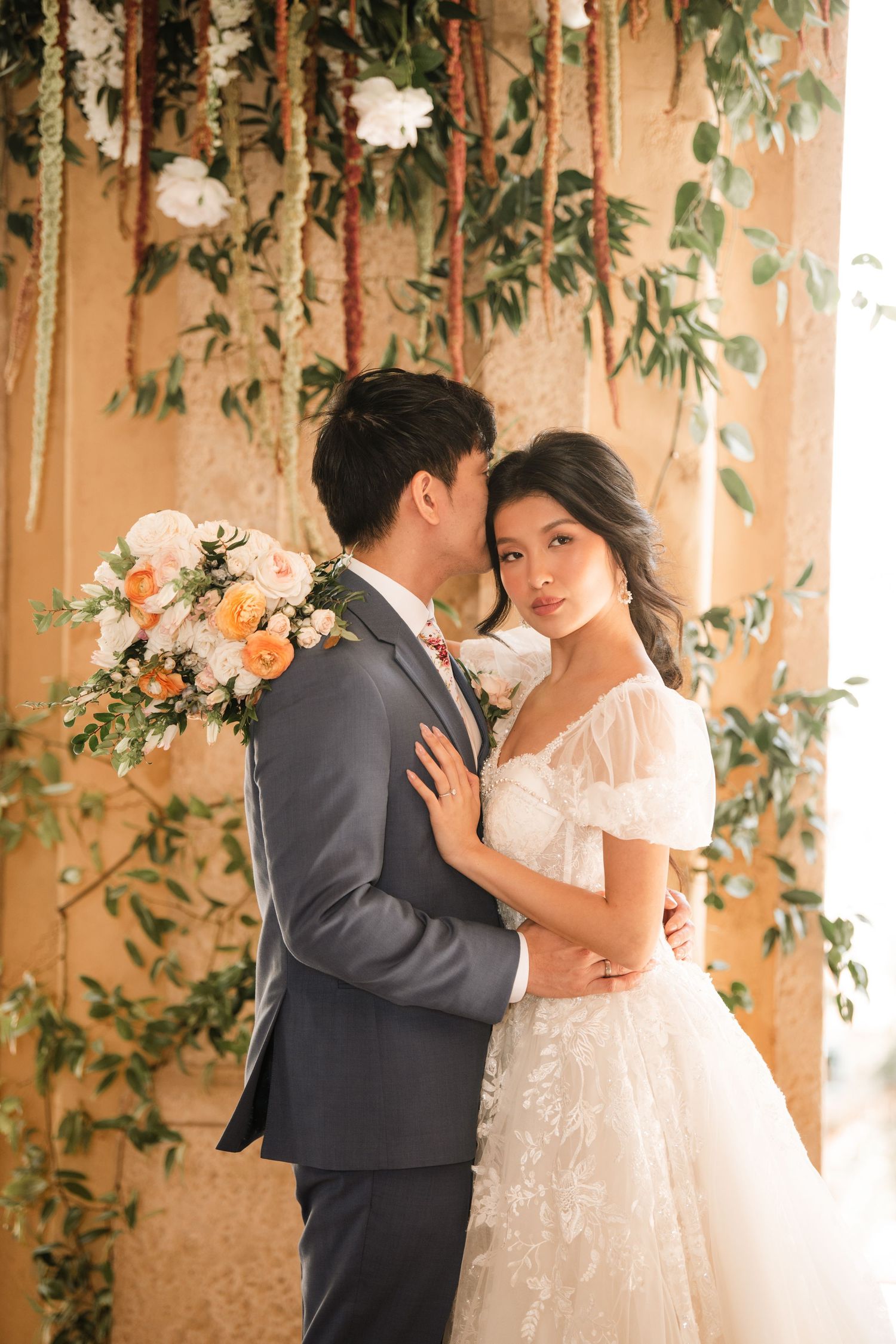 Intimate wedding moment captured under floral-decorated stone columns.