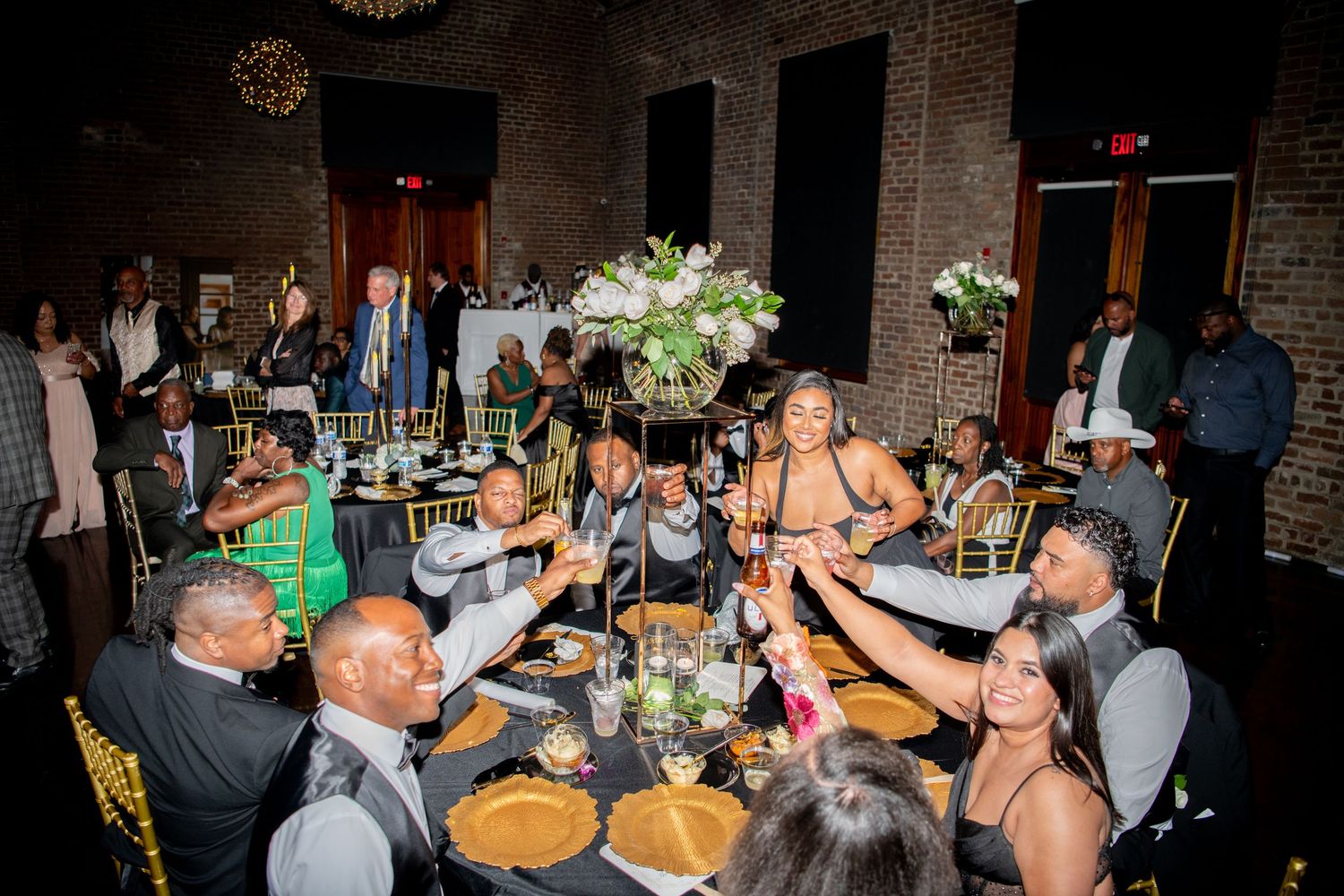 Reception guests toasting and celebrating at decorated tables in an industrial-style venue.