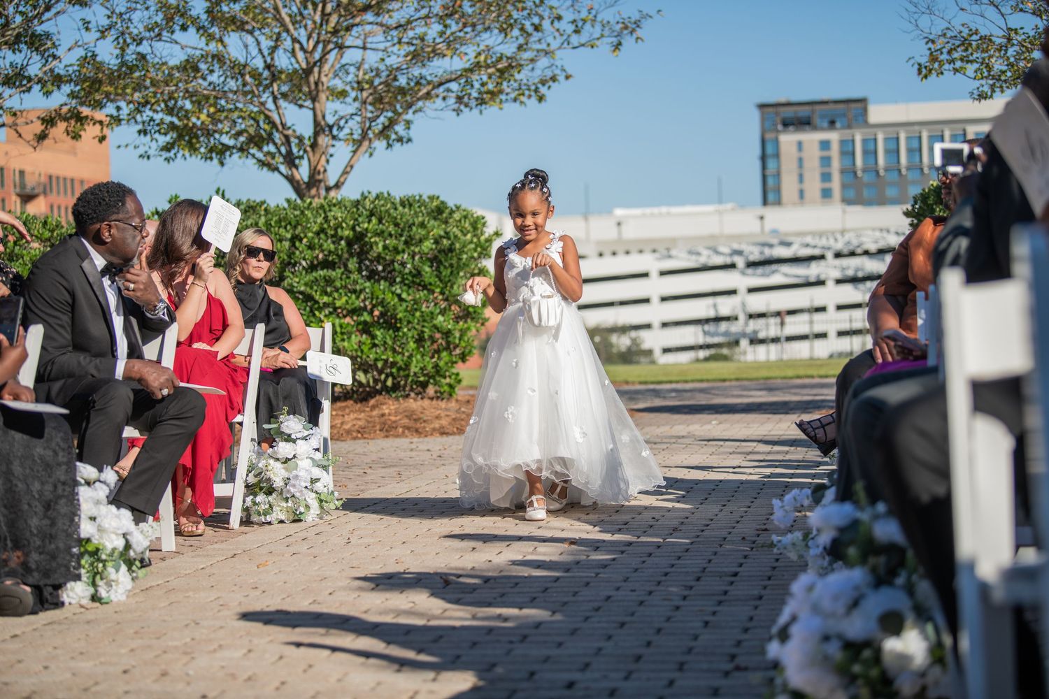 Outdoor wedding ceremony setup with guests seated on white chairs.