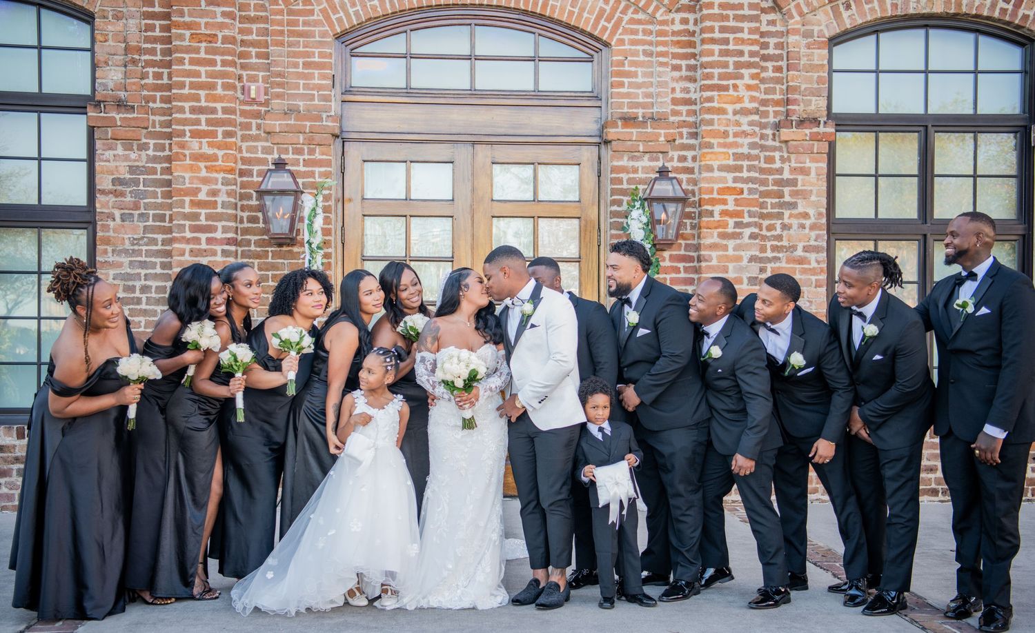 Extended panoramic photo of formal wedding party gathered outside historic brick building.