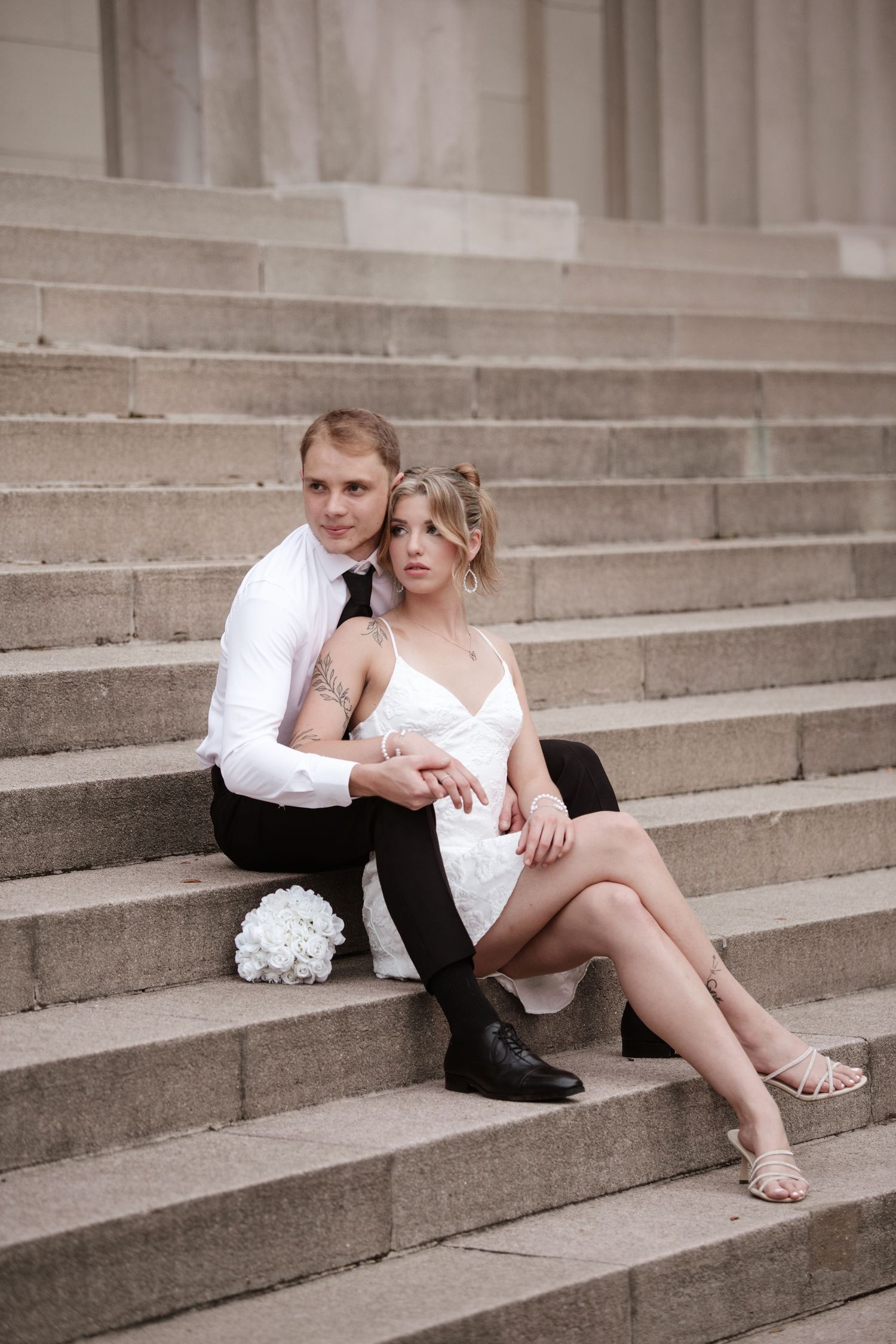 A couple in black and white attire poses romantically on wide stone steps.