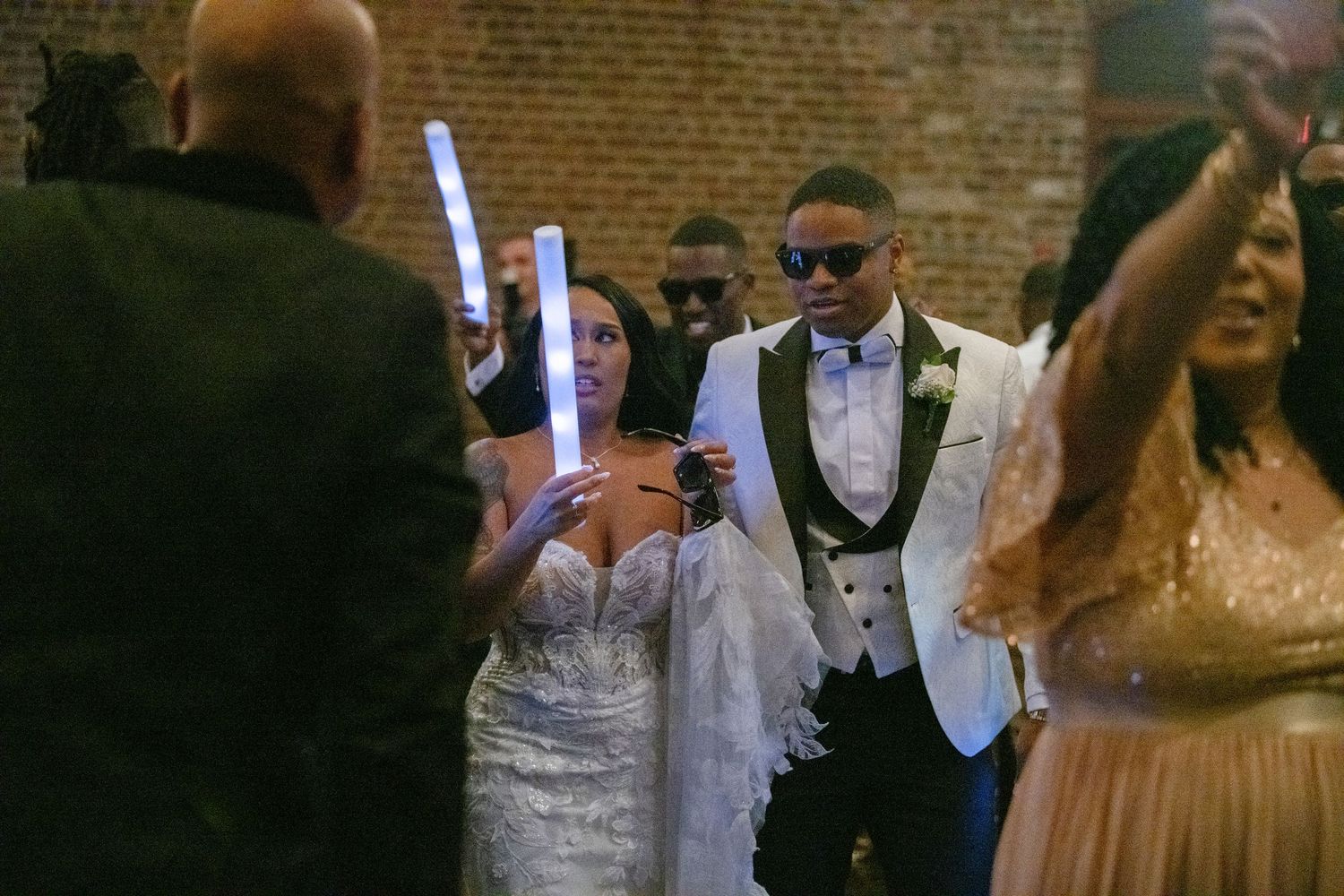 Wedding reception dance floor with guests in formal attire against brick walls.