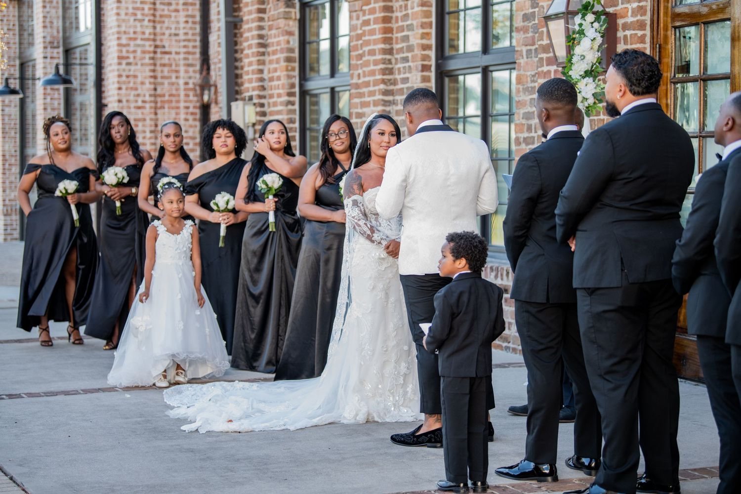 Wedding guests gather outside a brick venue building during an outdoor ceremony.