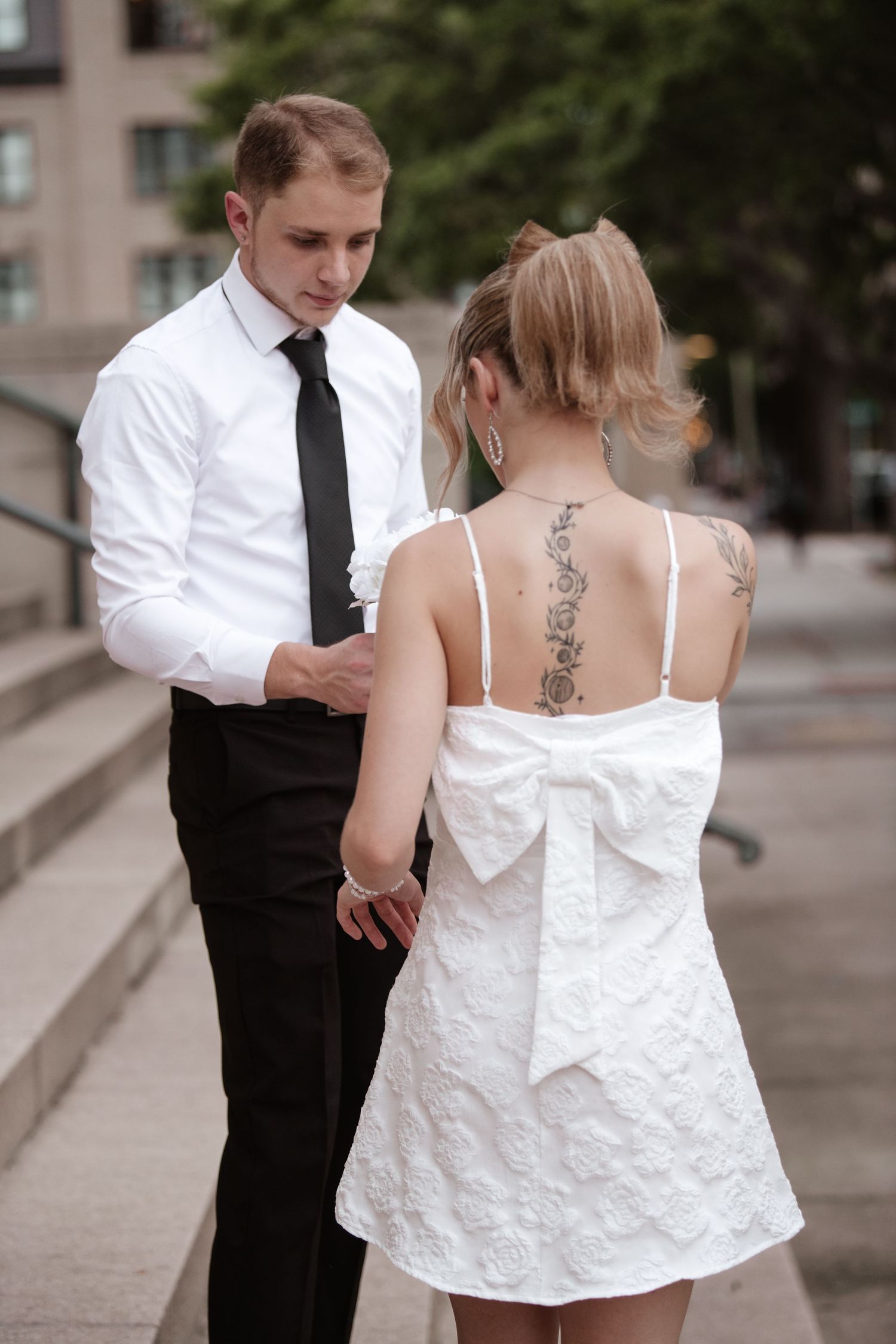 A couple in formal attire poses together near stone columns.