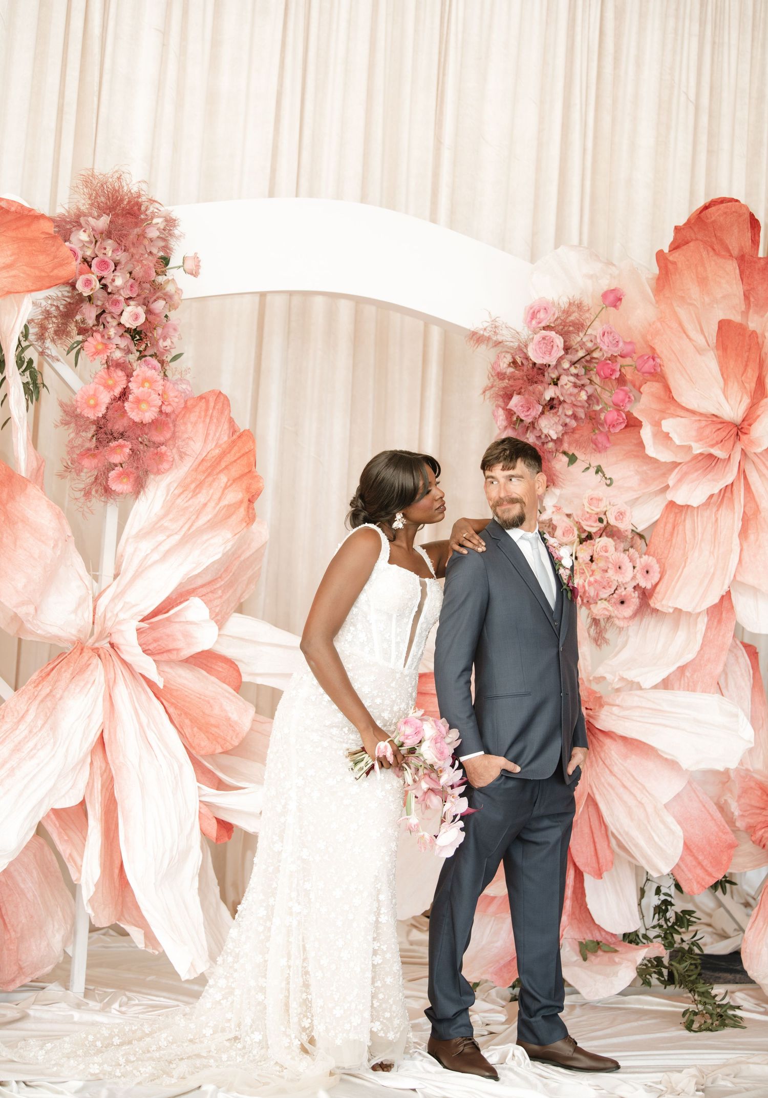 Series of romantic wedding poses with large coral flowers and white drapery.