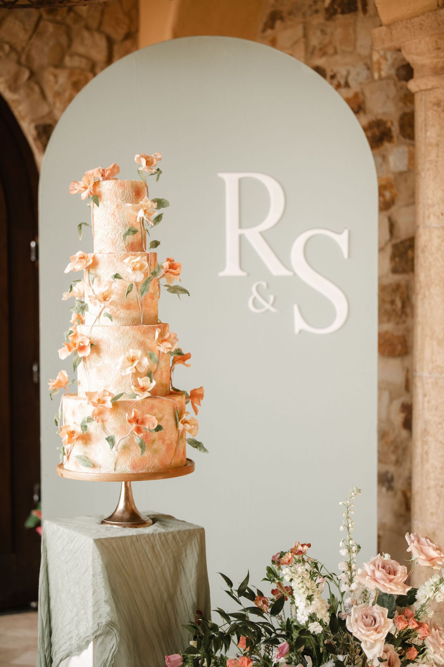 Elegant peach-colored wedding cake displayed against soft blue backdrop with monogram letters.