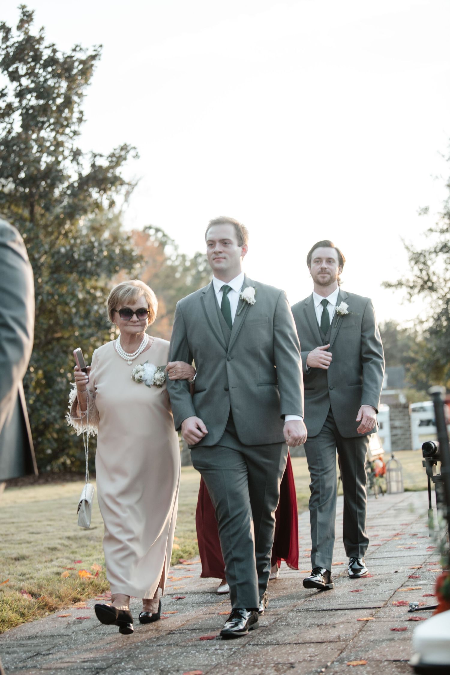 Wedding party members walk down an outdoor path during a formal ceremony.