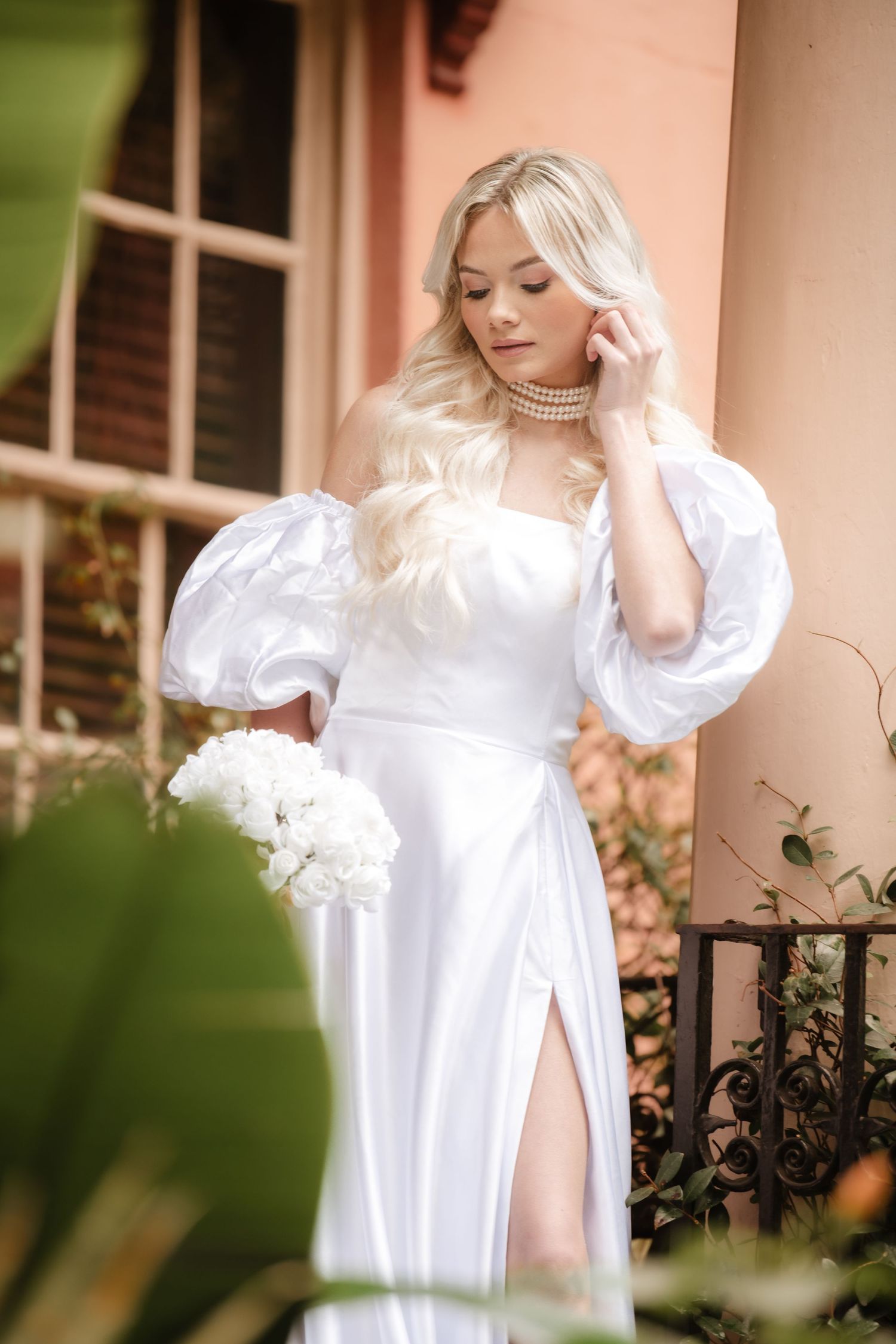 Elegant white wedding dress with puff sleeves and thigh slit photographed in romantic outdoor garden setting.