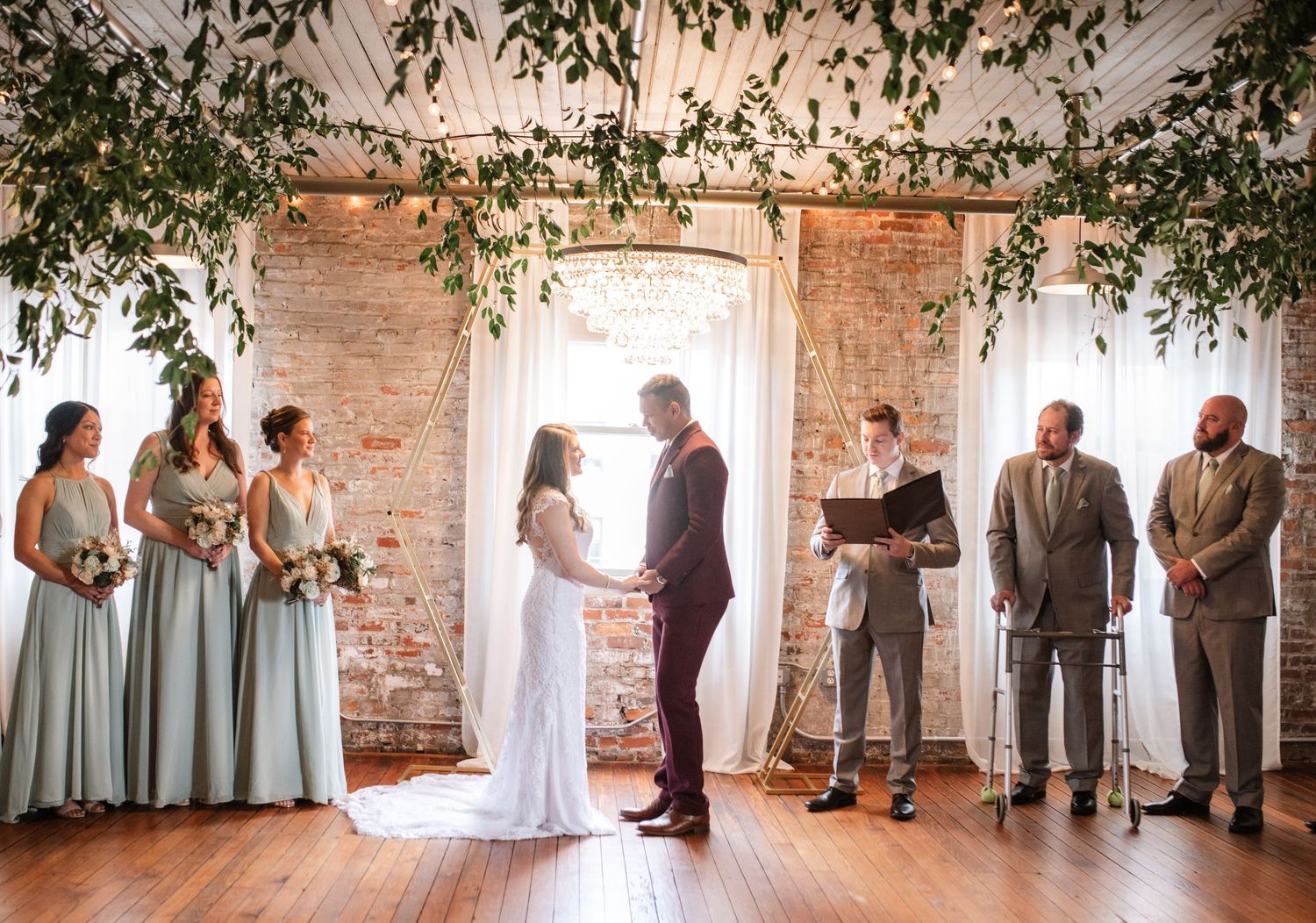 Wedding party lined up in a rustic brick venue with natural light streaming through windows.