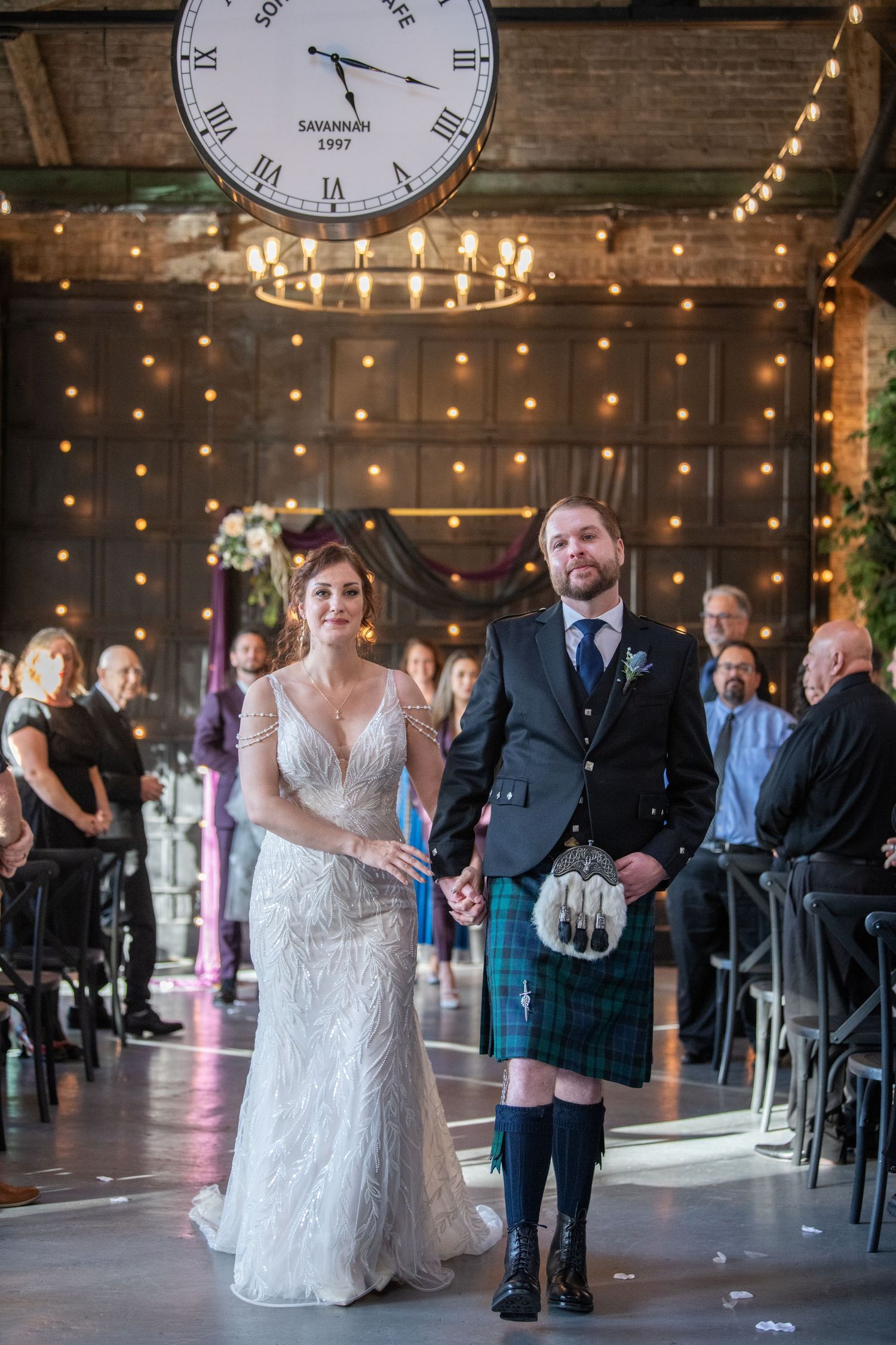 Wedding celebration in a rustic venue with string lights and guests dancing.