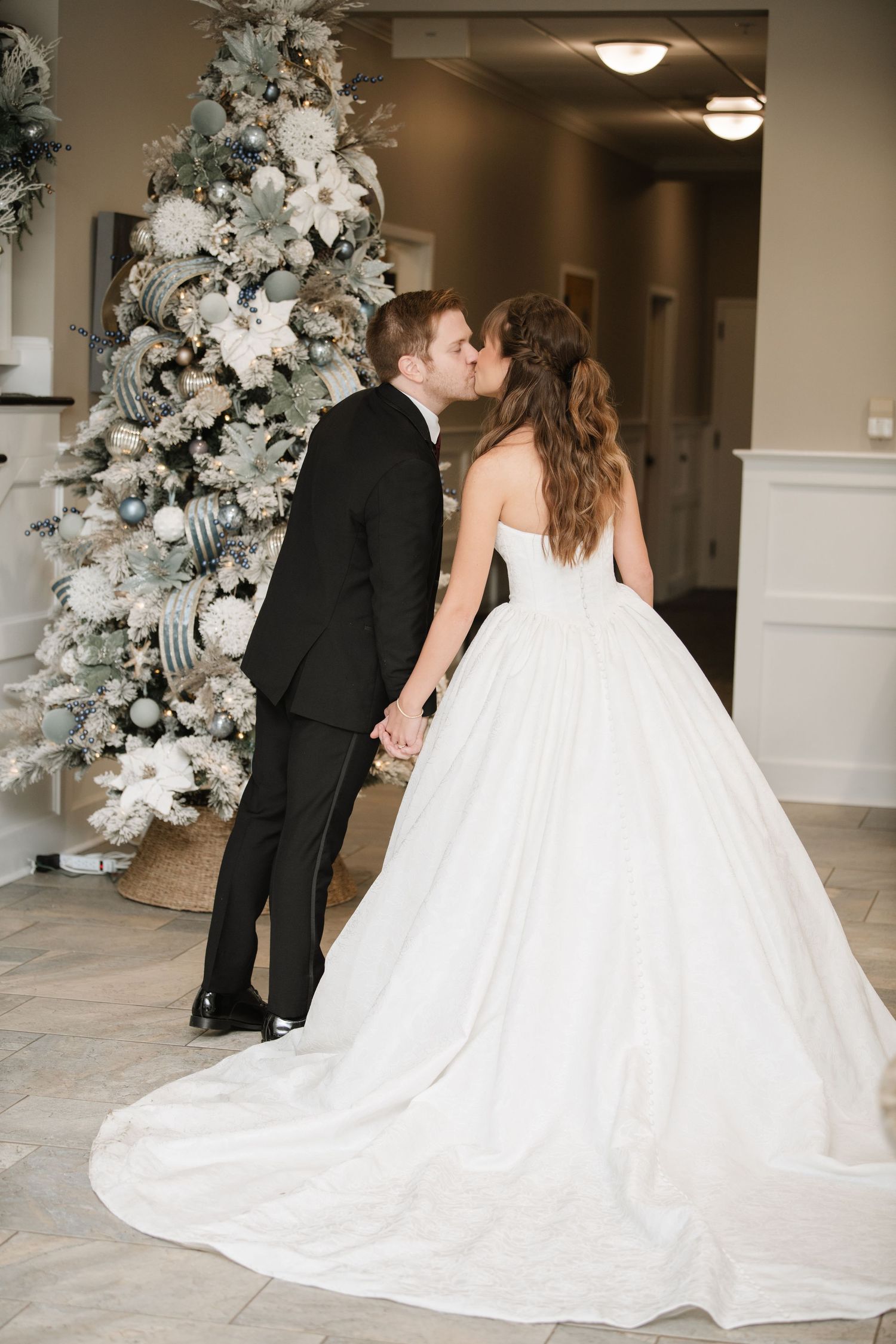 Wedding couple poses near decorated Christmas tree in elegant indoor setting.