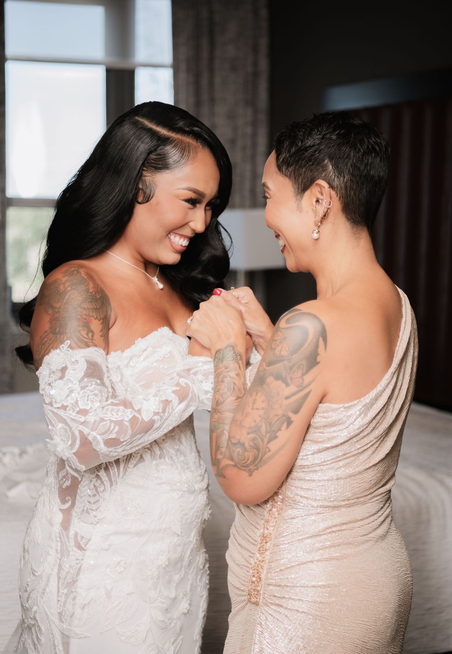 Two people share a joyful moment in elegant white and champagne wedding dresses.