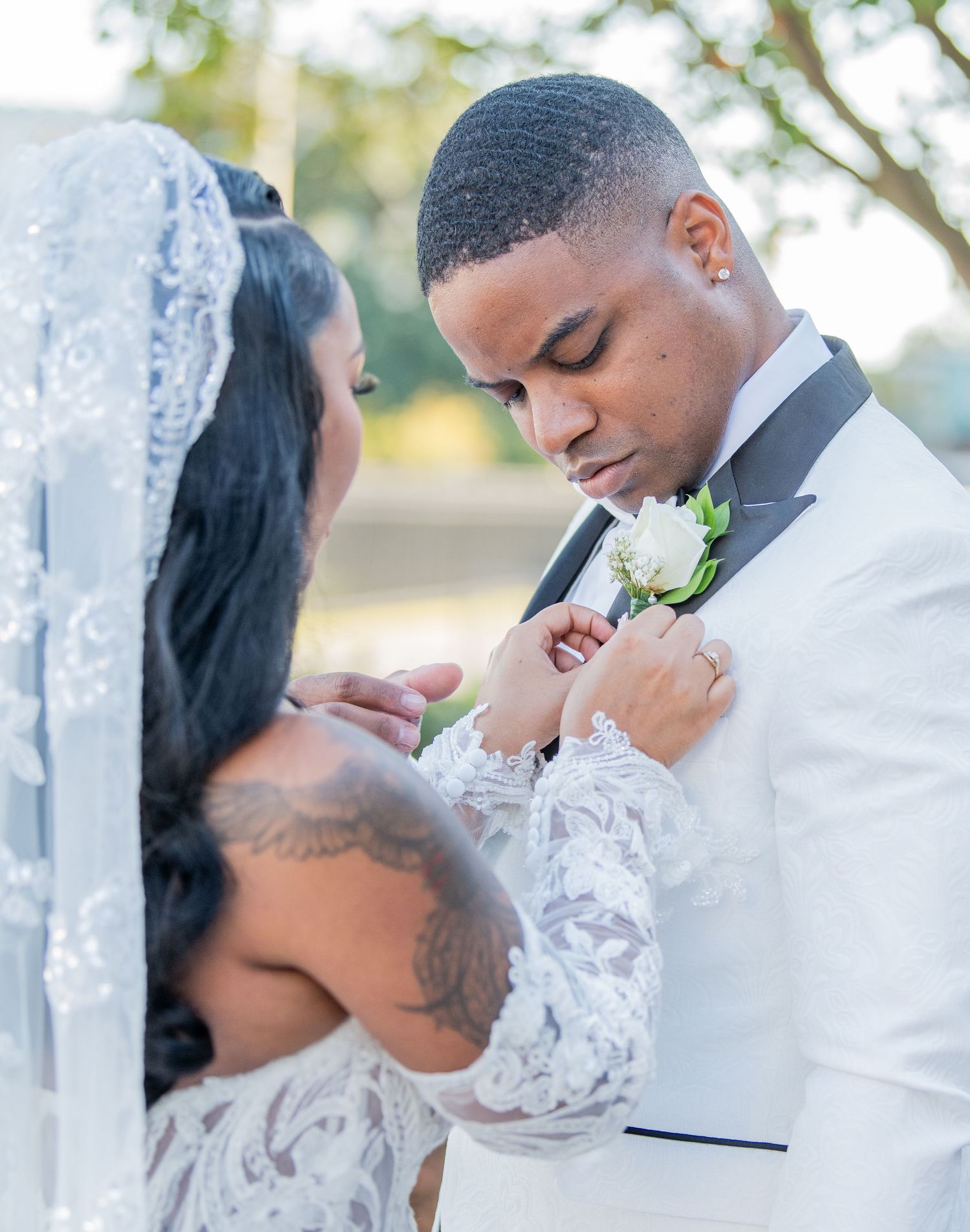 Tender wedding moments captured outdoors with elegant white attire and lace details.