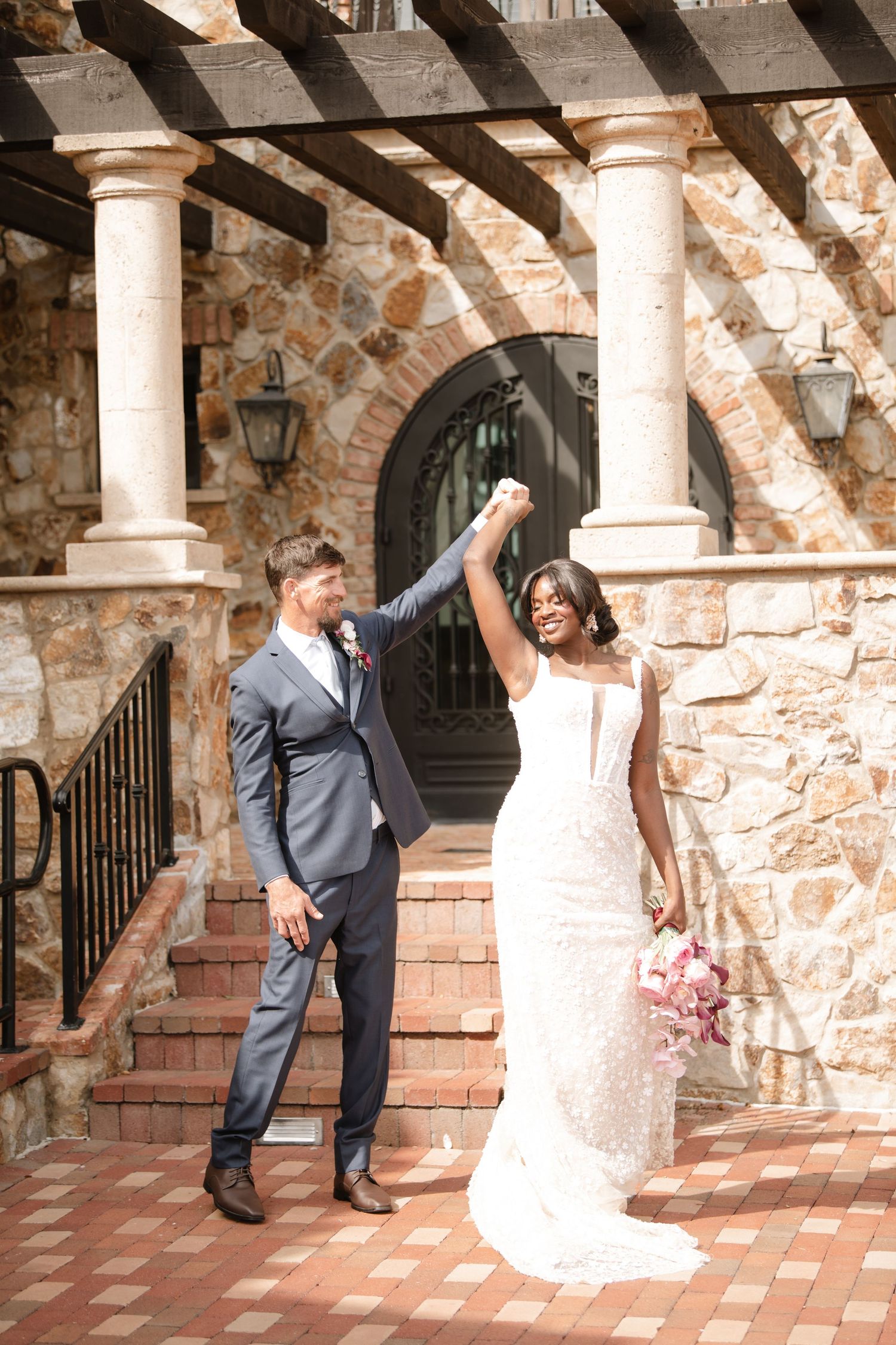 Playful wedding couple poses under stone archway with columns.