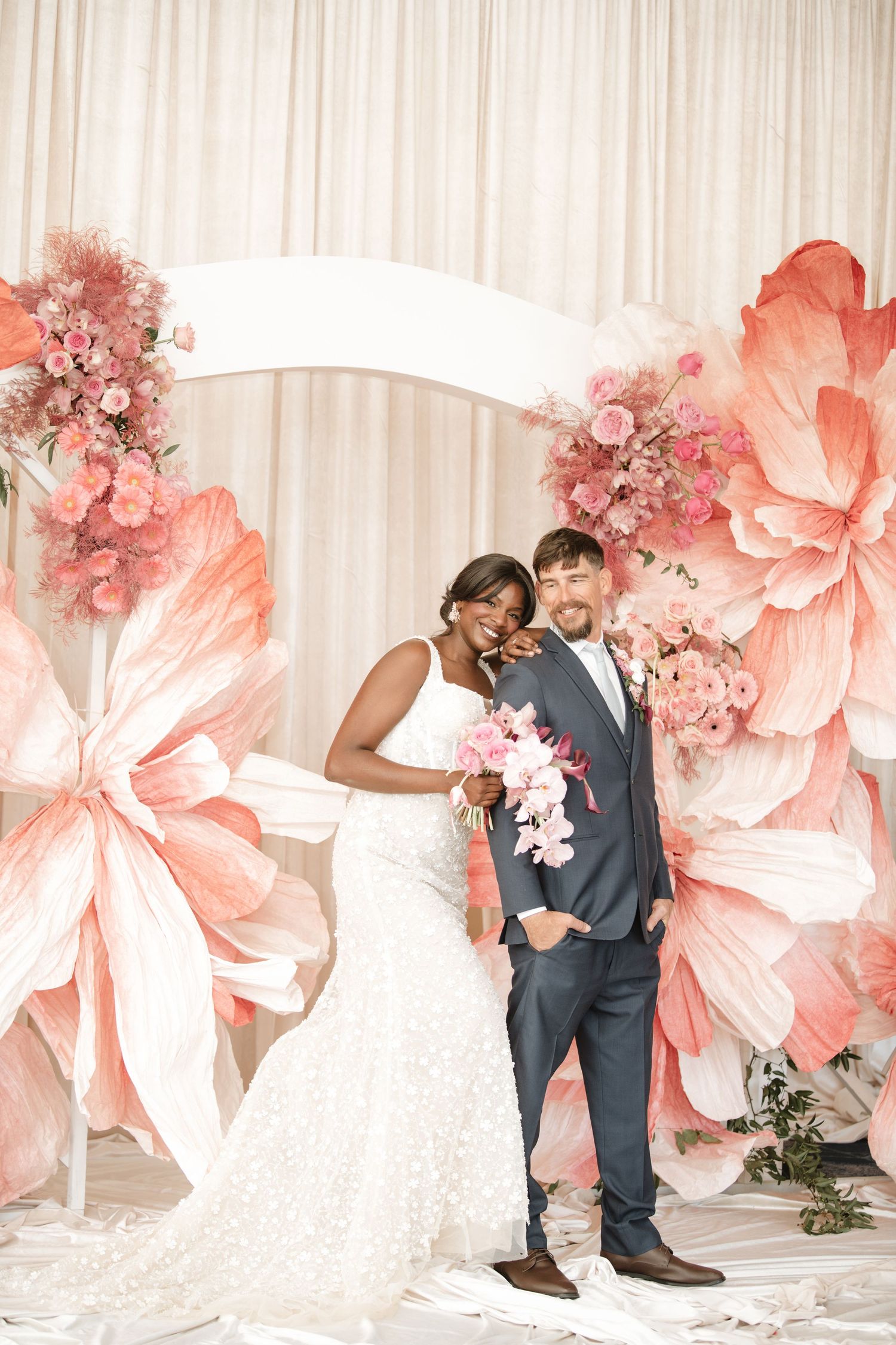 Sequence of romantic wedding poses against a backdrop of oversized coral paper flowers.