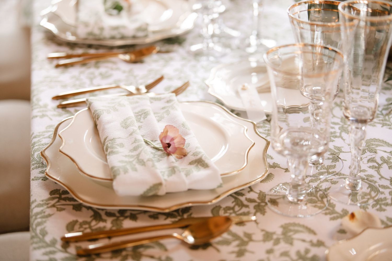 Close-up of luxurious place settings with gold cutlery and crystal glassware on white tablecloth.