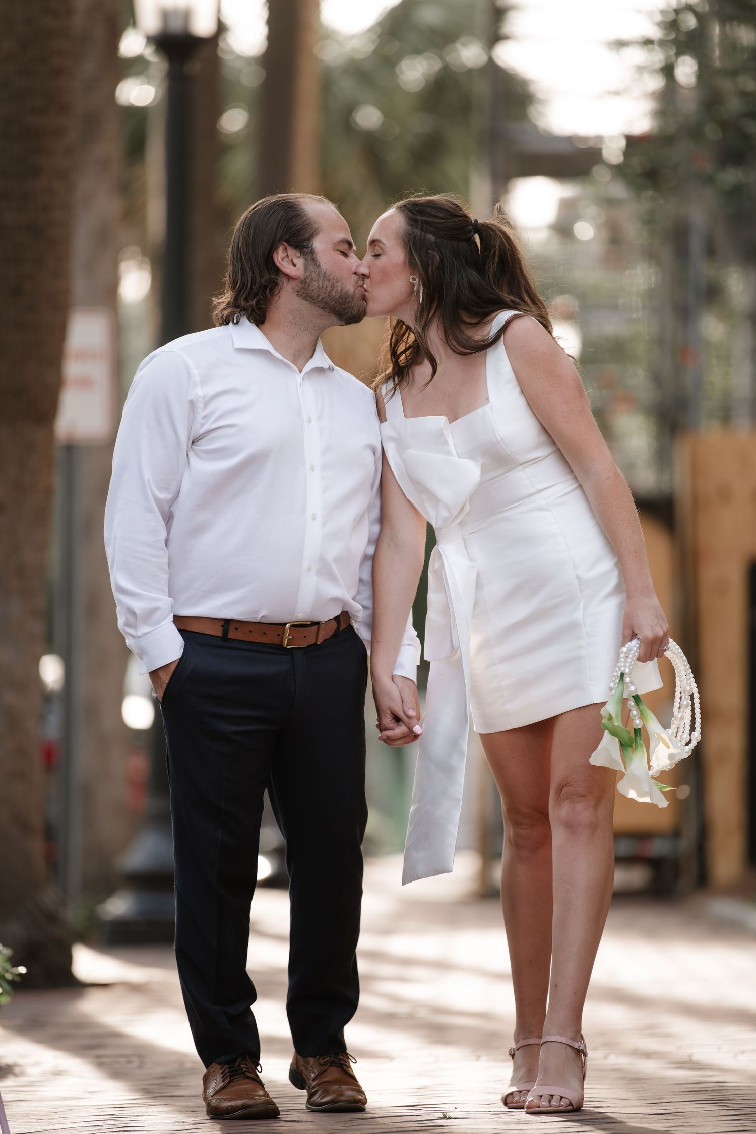 A romantic couple in white and black attire share intimate moments in a sunlit outdoor setting.