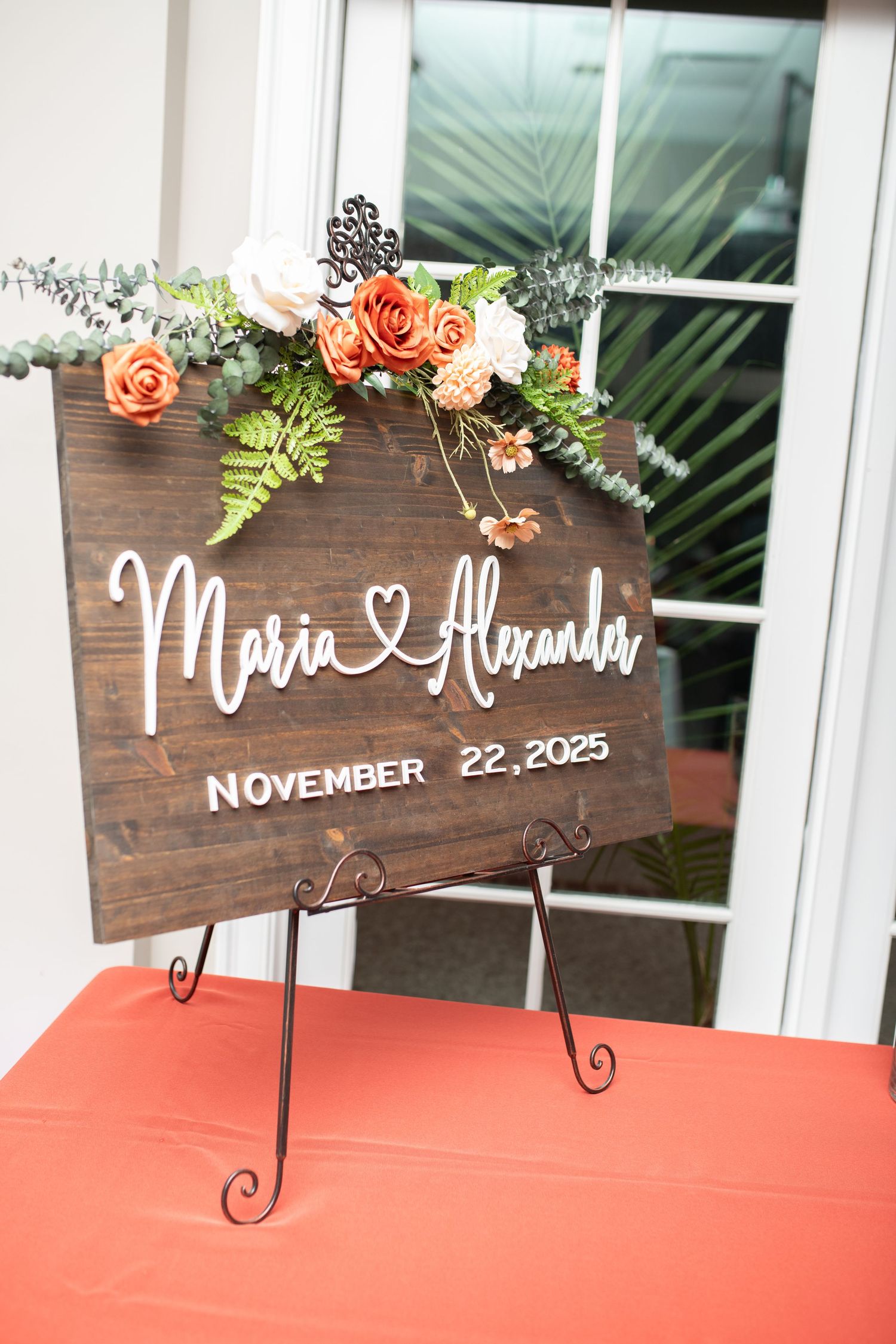 Rustic wooden wedding welcome sign decorated with coral flowers and greenery.