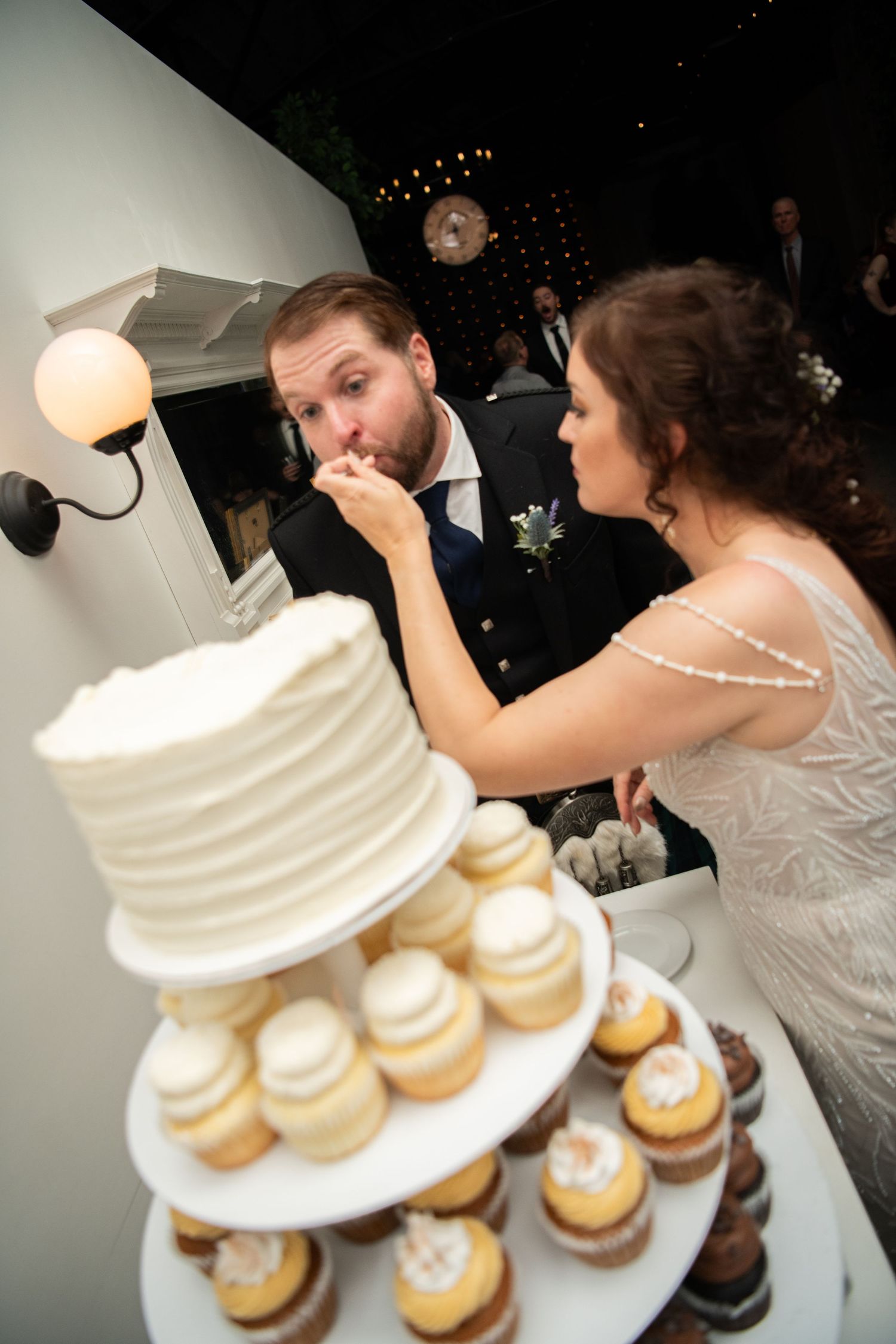 Couple sharing wedding cake and cupcakes at dessert table.