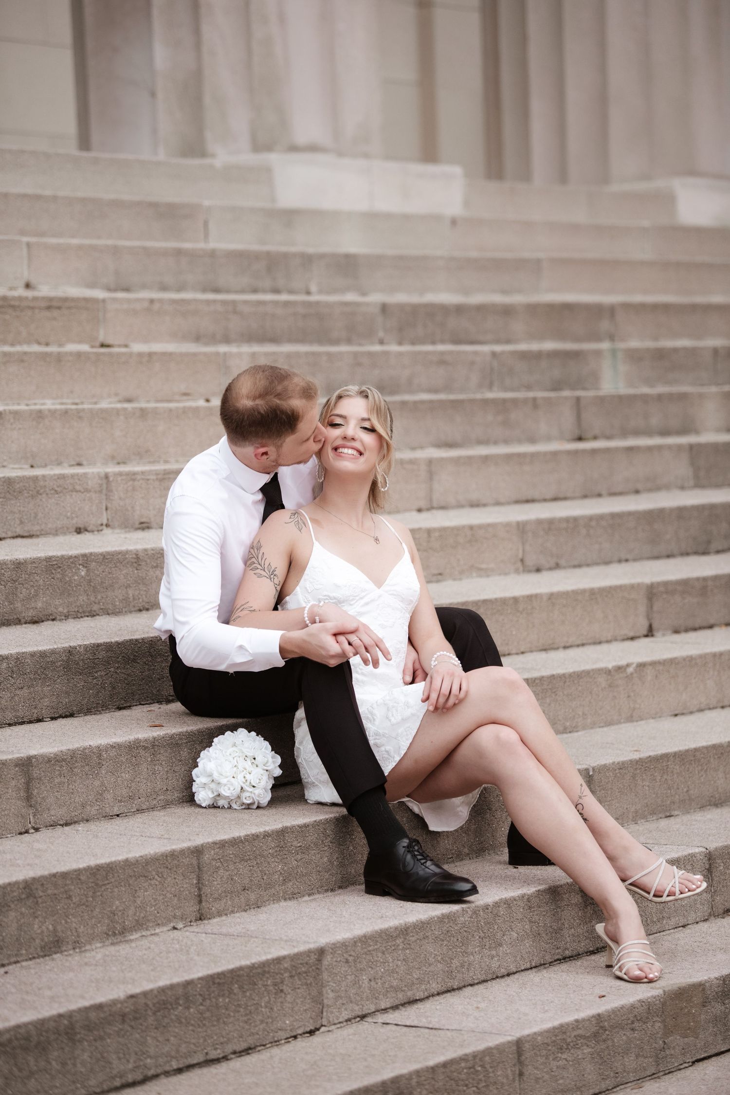 A romantic couple in contrasting black and white outfits embraces on concrete stairs.