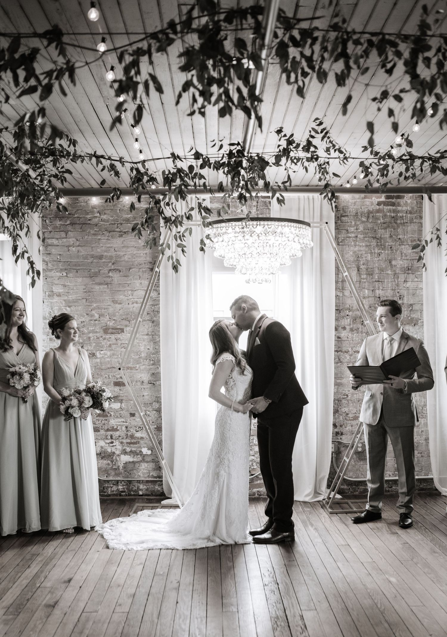 Wedding ceremony in a bright industrial space with exposed brick walls and hanging greenery.