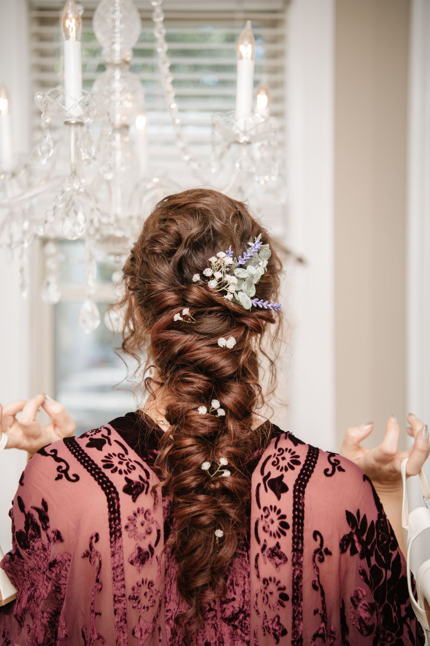 Elegant braided hairstyles adorned with crystal accessories and flowers against chandelier lighting.