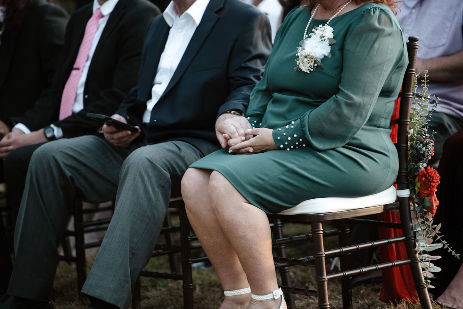 Guests seated in formal attire at an outdoor wedding ceremony.