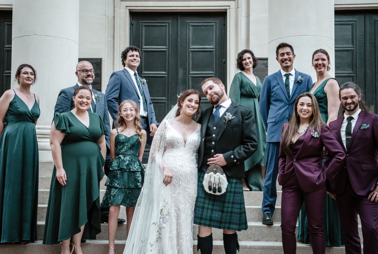 Wedding party group photo with bridesmaids and groomsmen in purple and green attire.