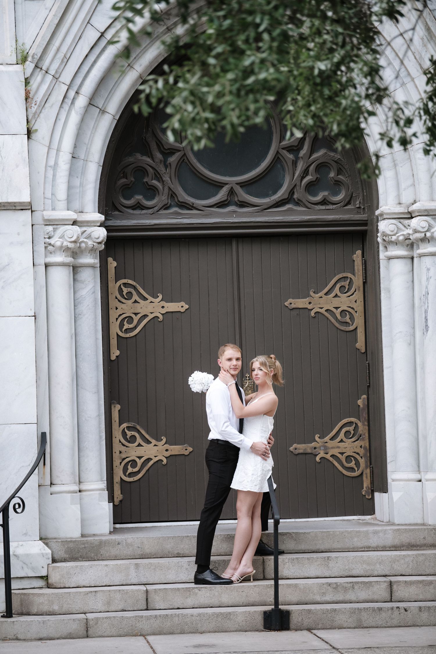 Couple poses playfully near ornate gothic archways and doors of a historic building.