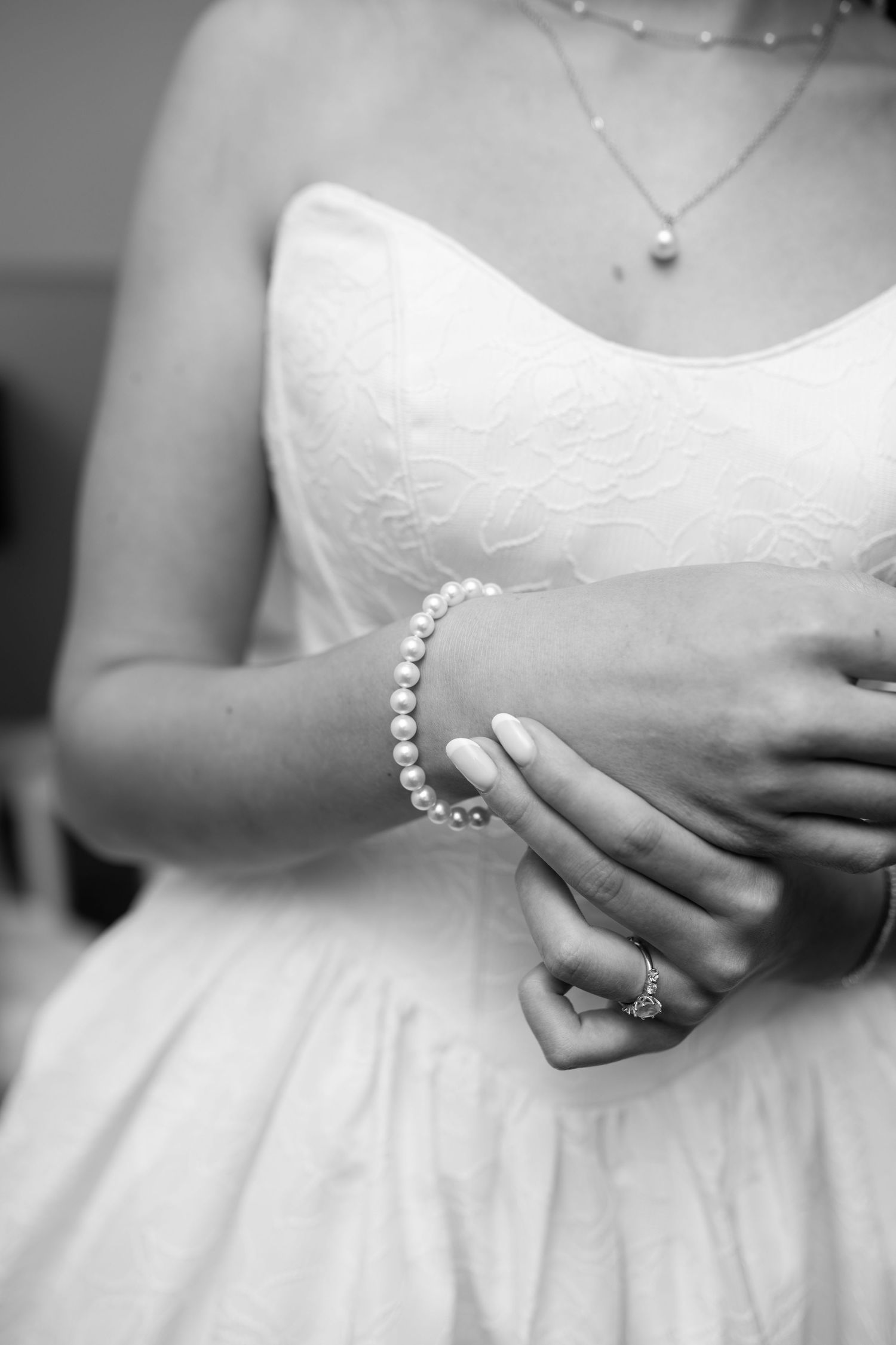 Close-up black and white photo of a bride's pearl bracelet and lace wedding dress details.