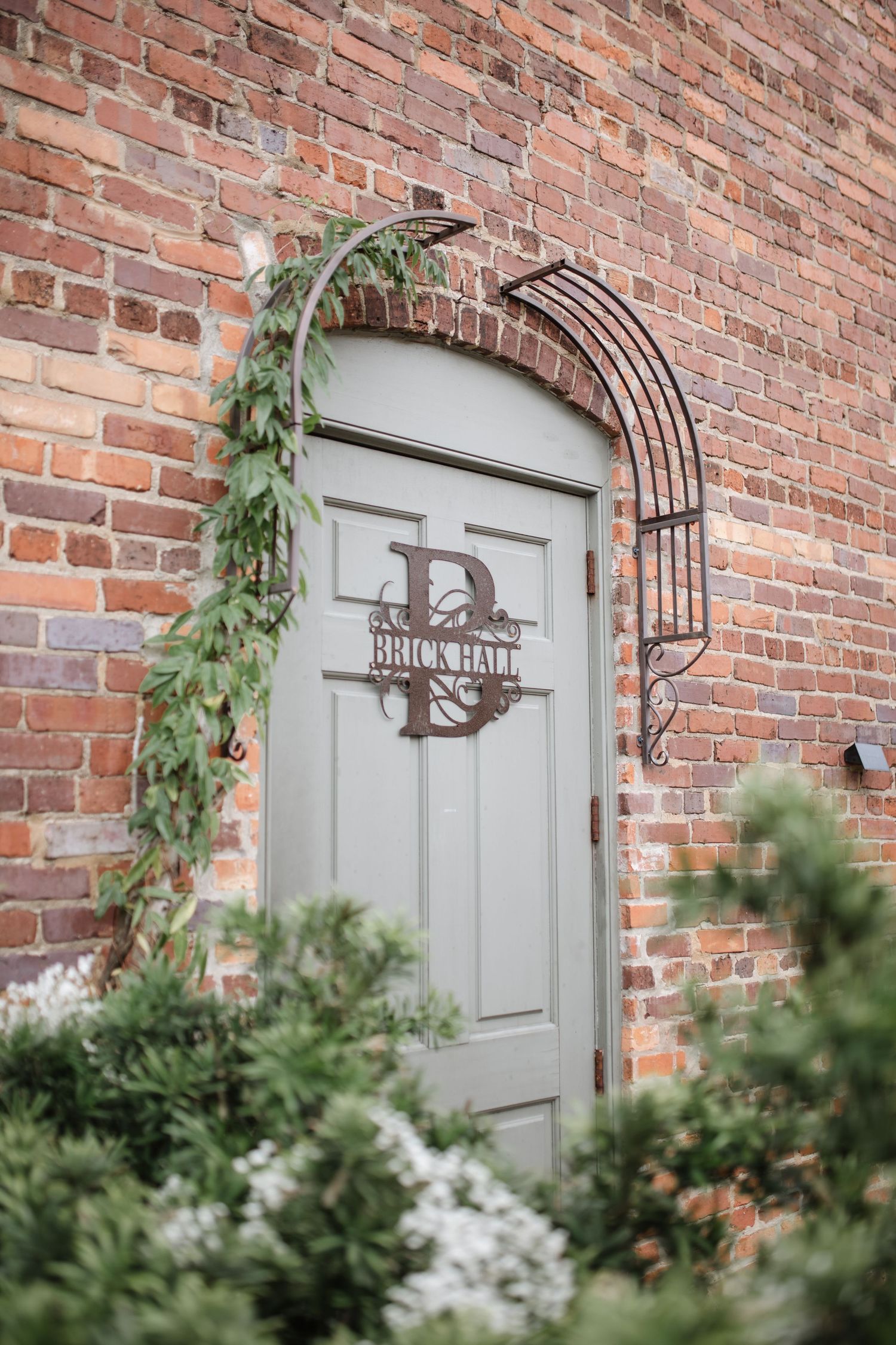 Grey doors with decorative metal arches set in red brick wall adorned with climbing plants.