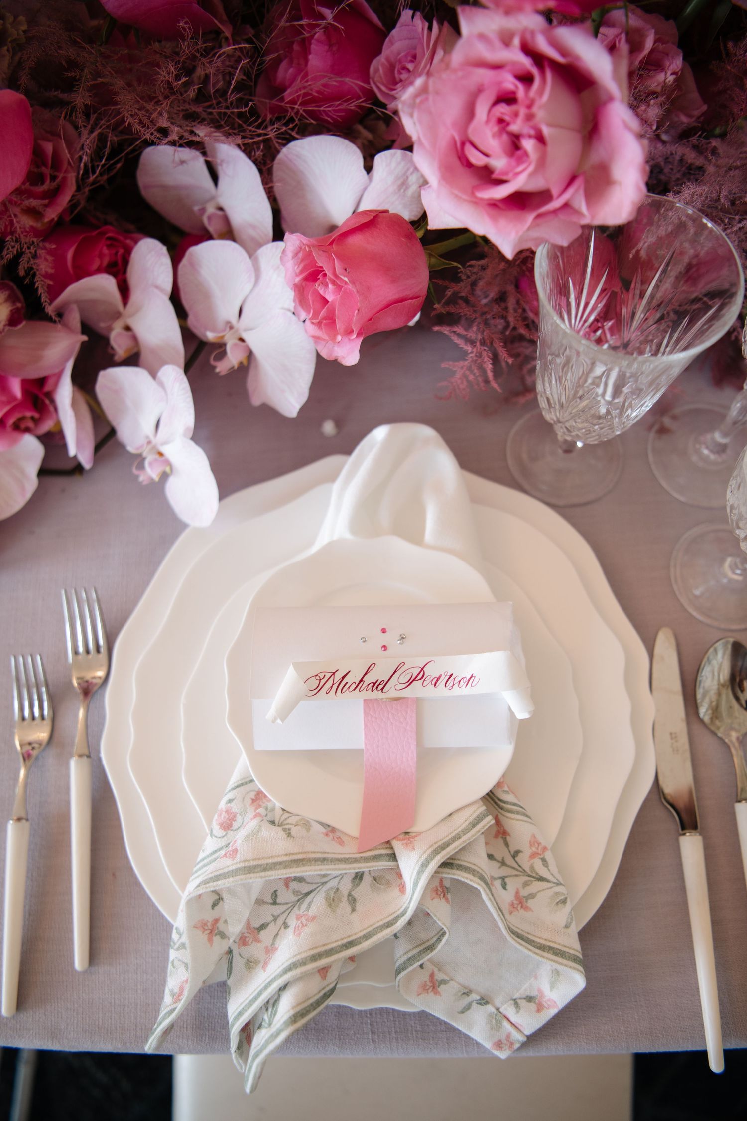 Elegant place settings with white plates, pink floral details, and rose centerpieces.