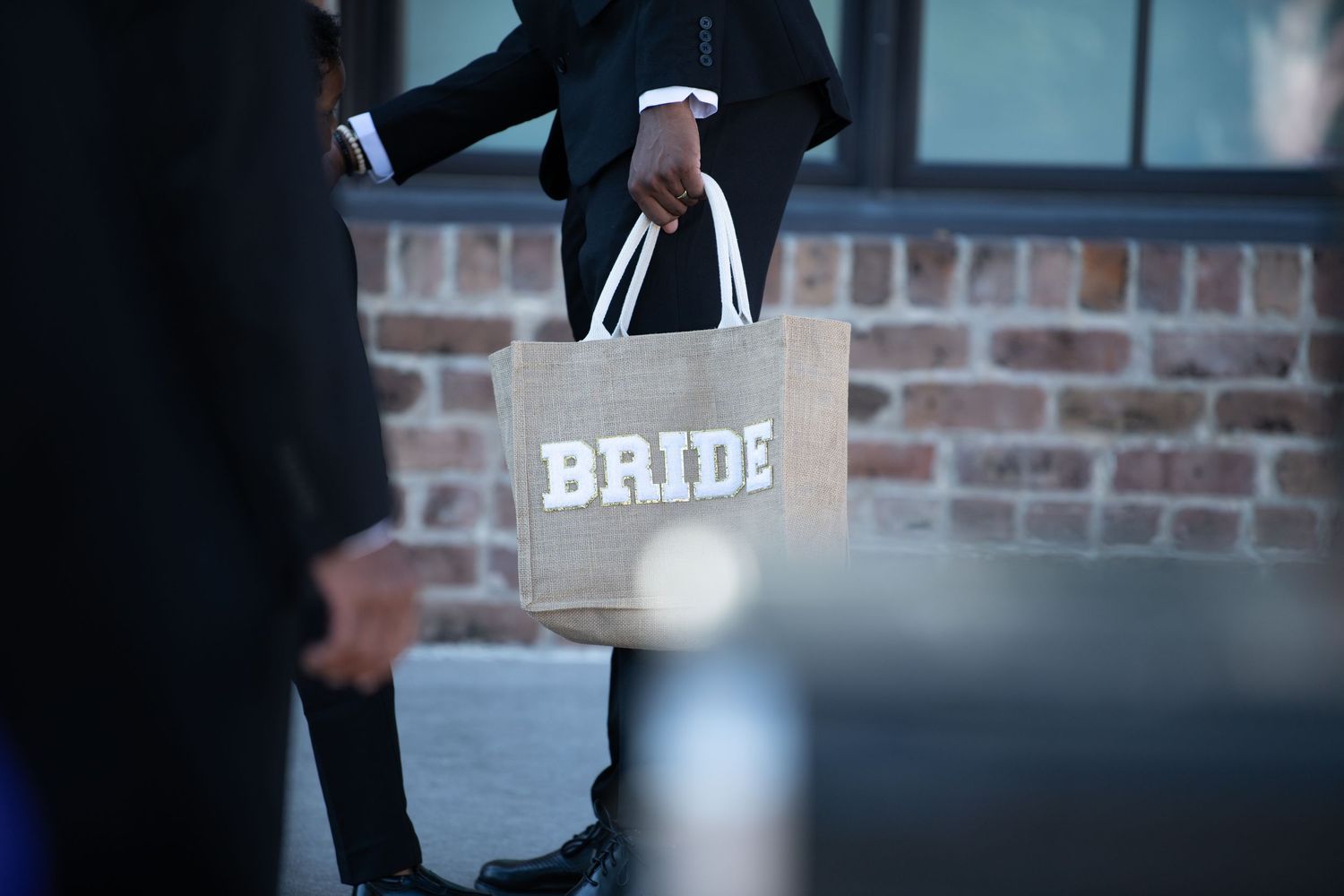 Wedding guests holding white gift bags and shopping bags outside a brick venue.