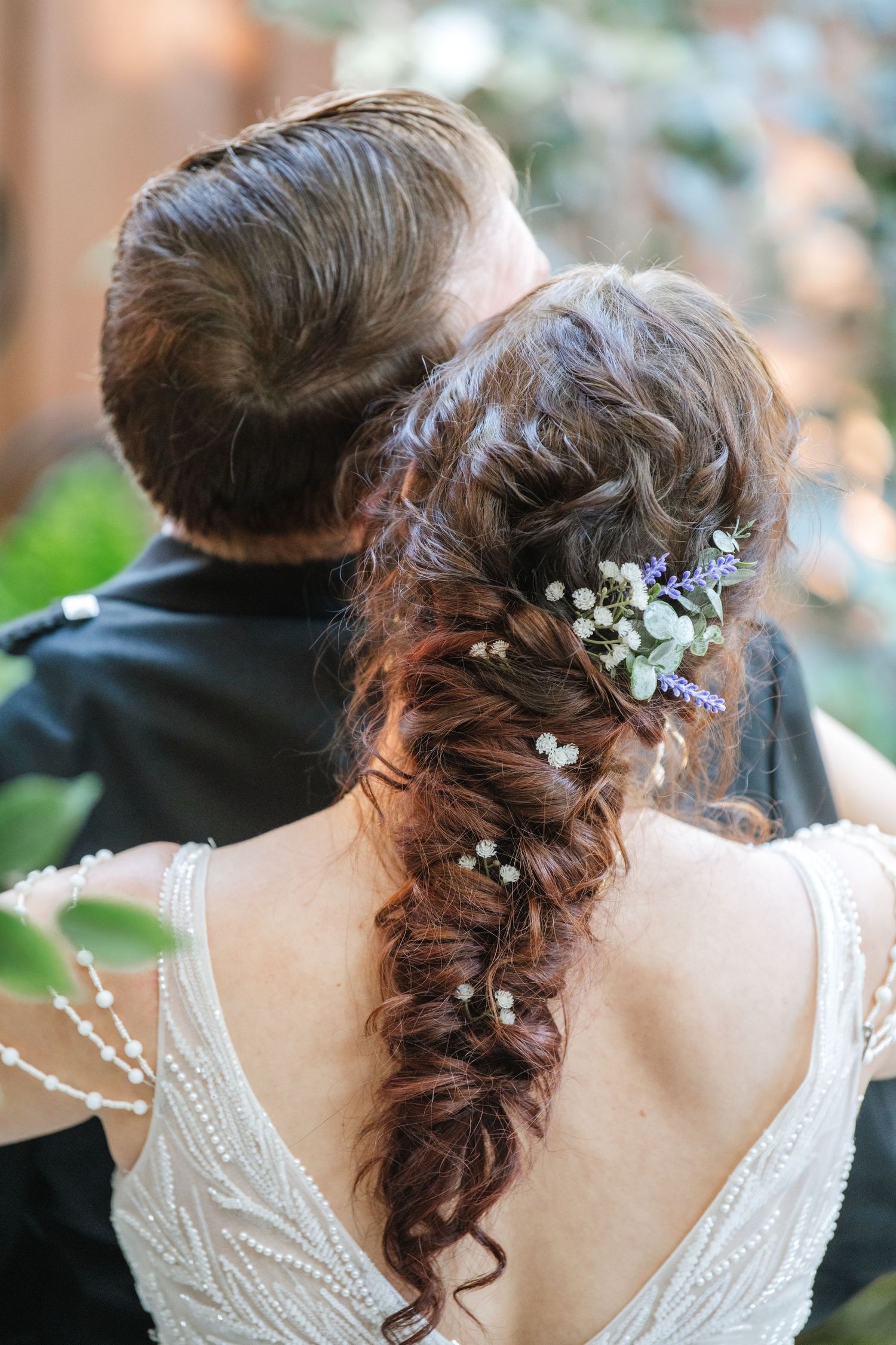 Close-up of a bride's intricate braided hairstyle adorned with delicate white flowers and greenery.