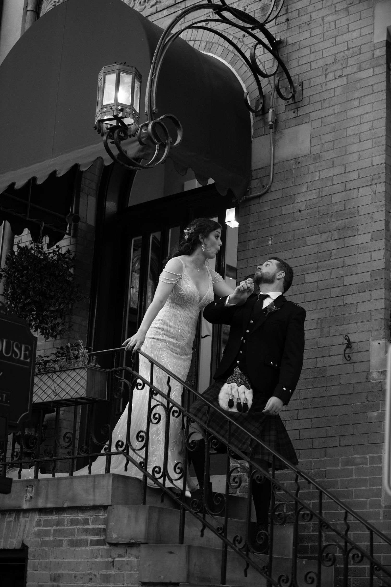 Black and white wedding portraits on the steps of a historic building with iron railings.